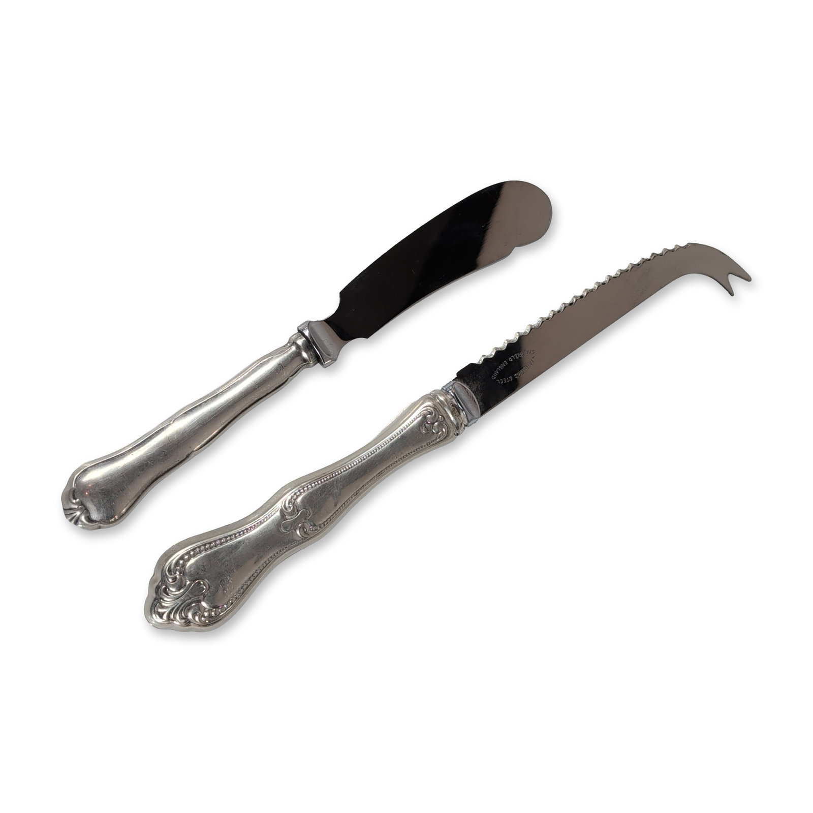 2pc Sterling Silver and Stainless Steel Spreader and Cheese Knives: Two serving knives with ornate shell and scroll patterned handles. One cheese knife featuring a serrated stainless steel blade with a curved, forked tip, marked Stainless Steel Sheffield England on th