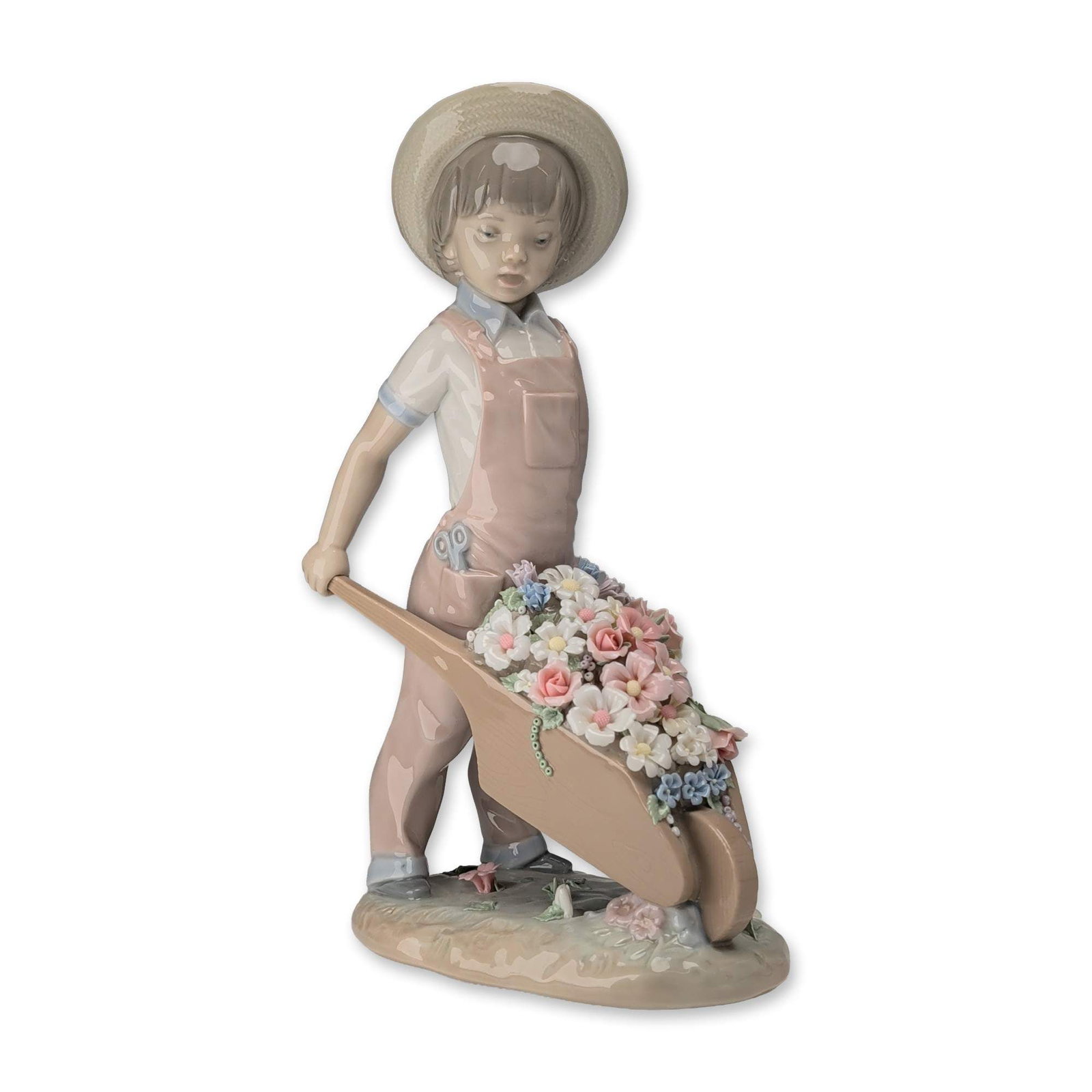 Lladro Spanish Porcelain Figurine Little Gardener 1283: Lladro glazed porcelain figurine titled Little Gardener, model number 1283. The piece depicts a young boy dressed in pink overalls and a straw hat pushing a rustic-style wheelbarrow filled with a vari