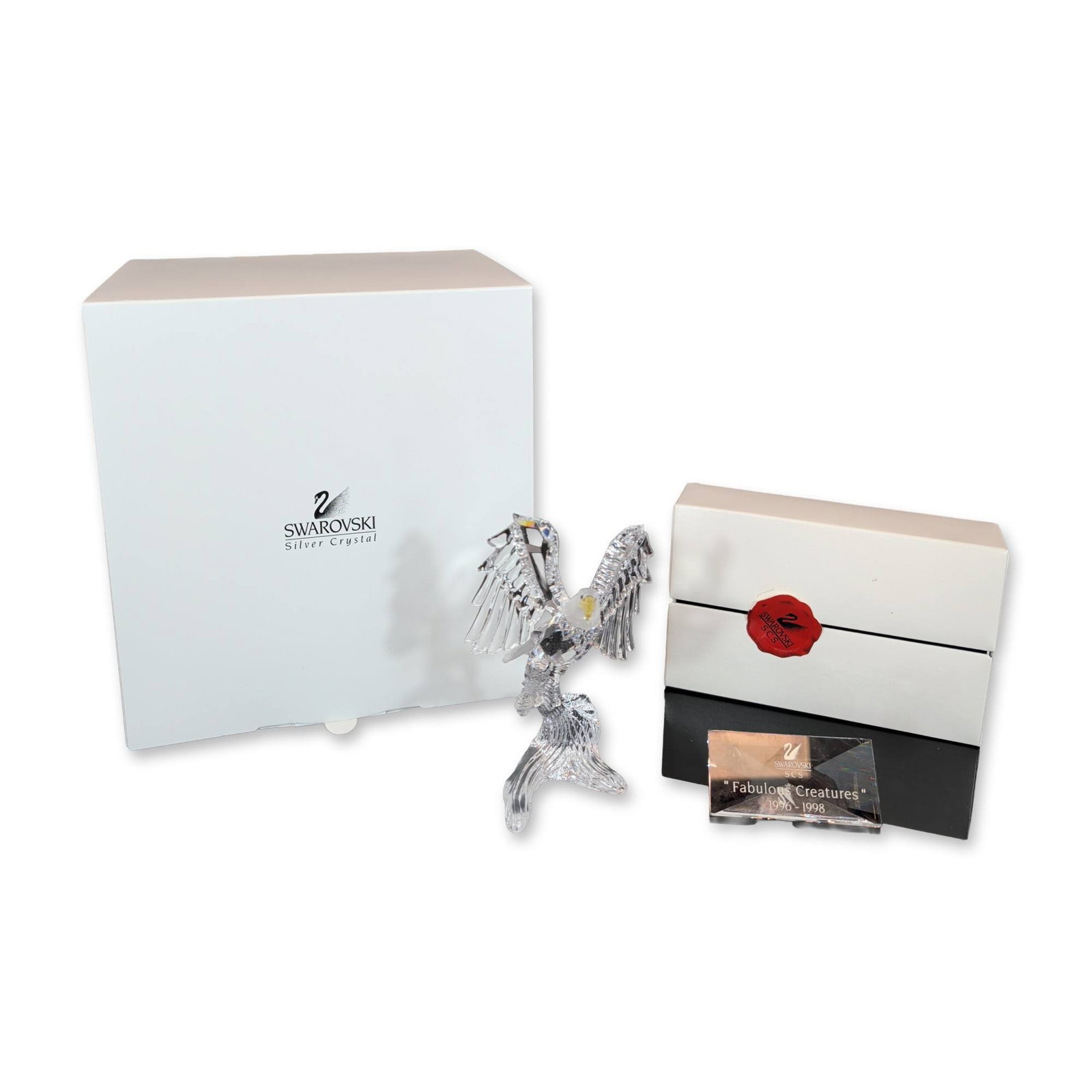 Swarovski Crystal Fabulous Creatures Bald Eagle Figurine with Plaque: The Bald Eagle features a faceted clear crystal body and outspread wings, contrasted by a frosted crystal head and tail feathers. The beak is rendered in faceted yellow-tinted crystal. Perched on a cr