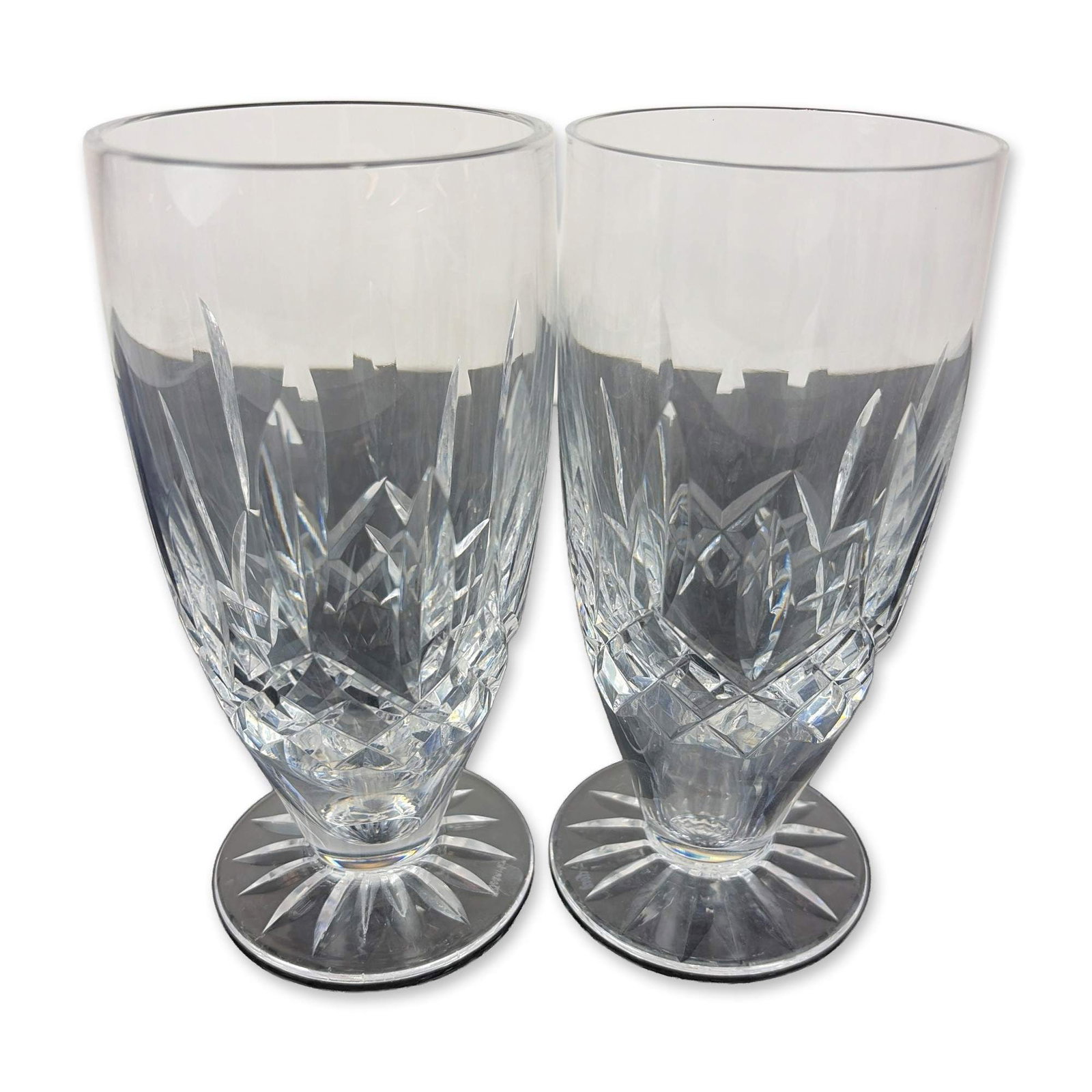 Pair of Waterford Lead Crystal Lismore Footed Iced Tea Glasses: Heavy lead crystal construction featuring a central band of diamond cuts flanked by vertical wedge cuts. The base of each glass exhibits a multi-point radial star cut. Both pieces bear the acid-etched