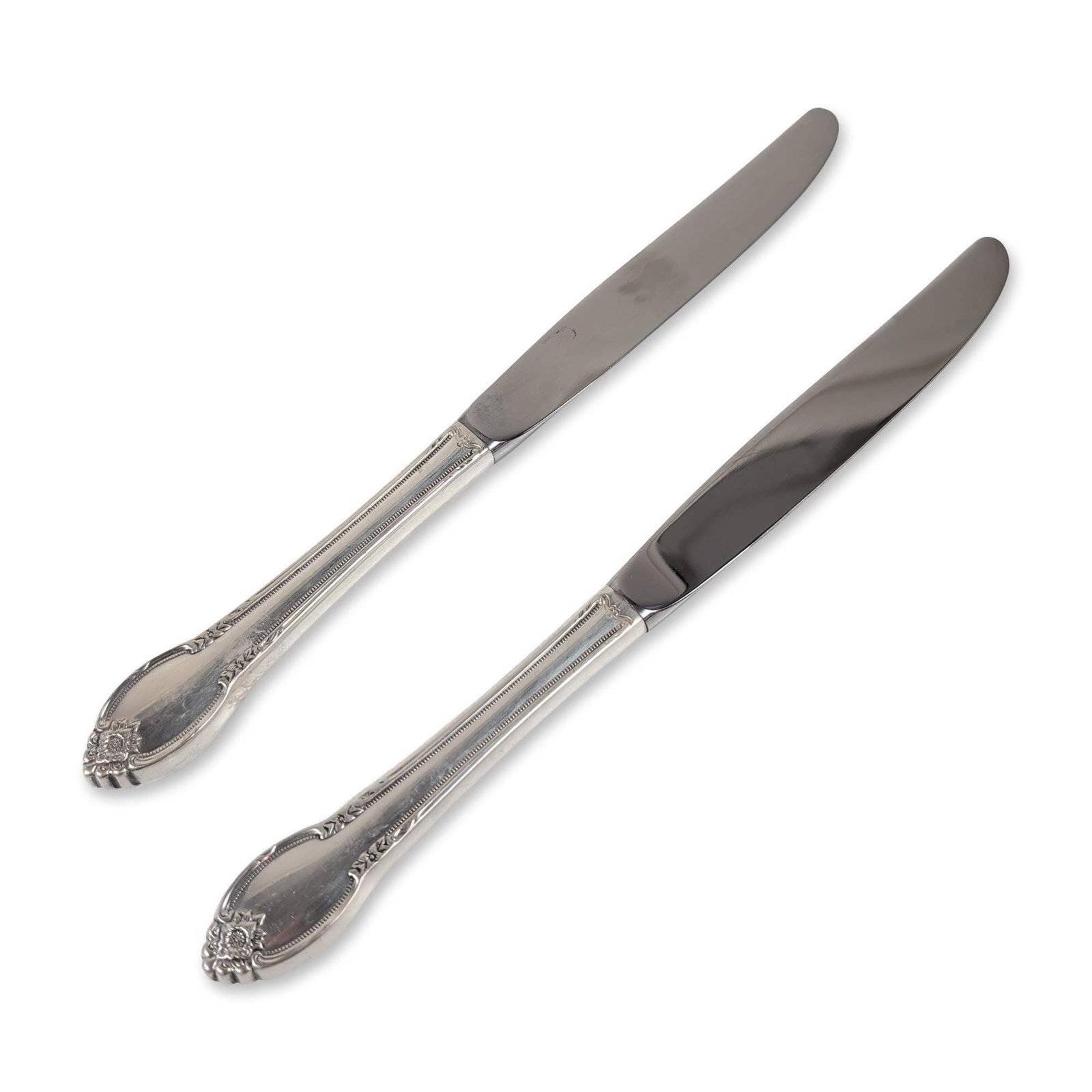 Pair of Ornate Sterling Silver Handle Knives: The handles are decorated with a rose motif at the terminal, accented by foliate scrolls and a continuous beaded border. The handles are fitted with polished stainless-steel blades. No monograms are p