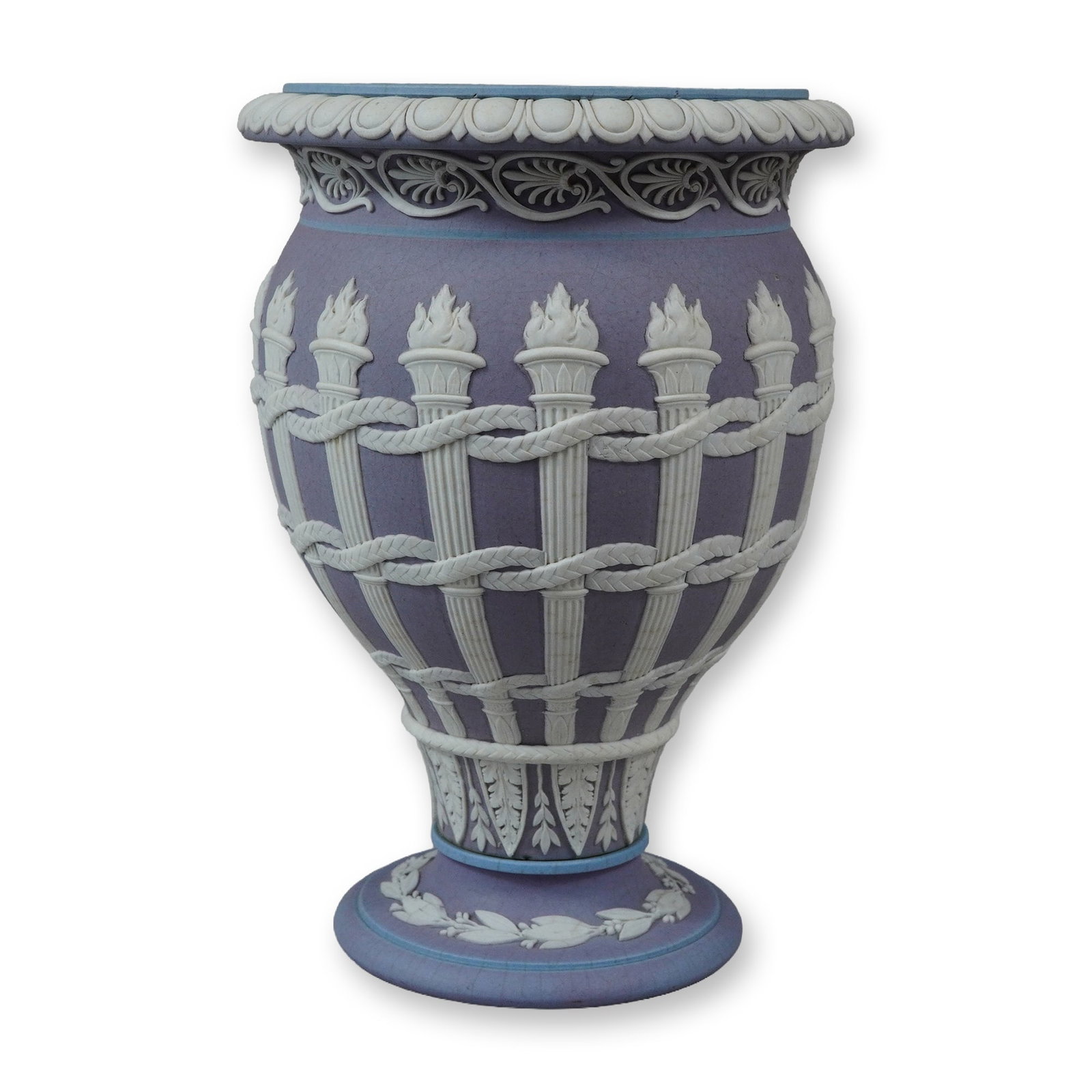 Wedgwood Tricolor Jasperware Dip Torch Motif Urn: A lilac-colored slip dip applied over a light blue stoneware body, which is visible along the interior rim and the edge of the foot. The vessel is ornamented with white sprigged reliefs. The flared ri