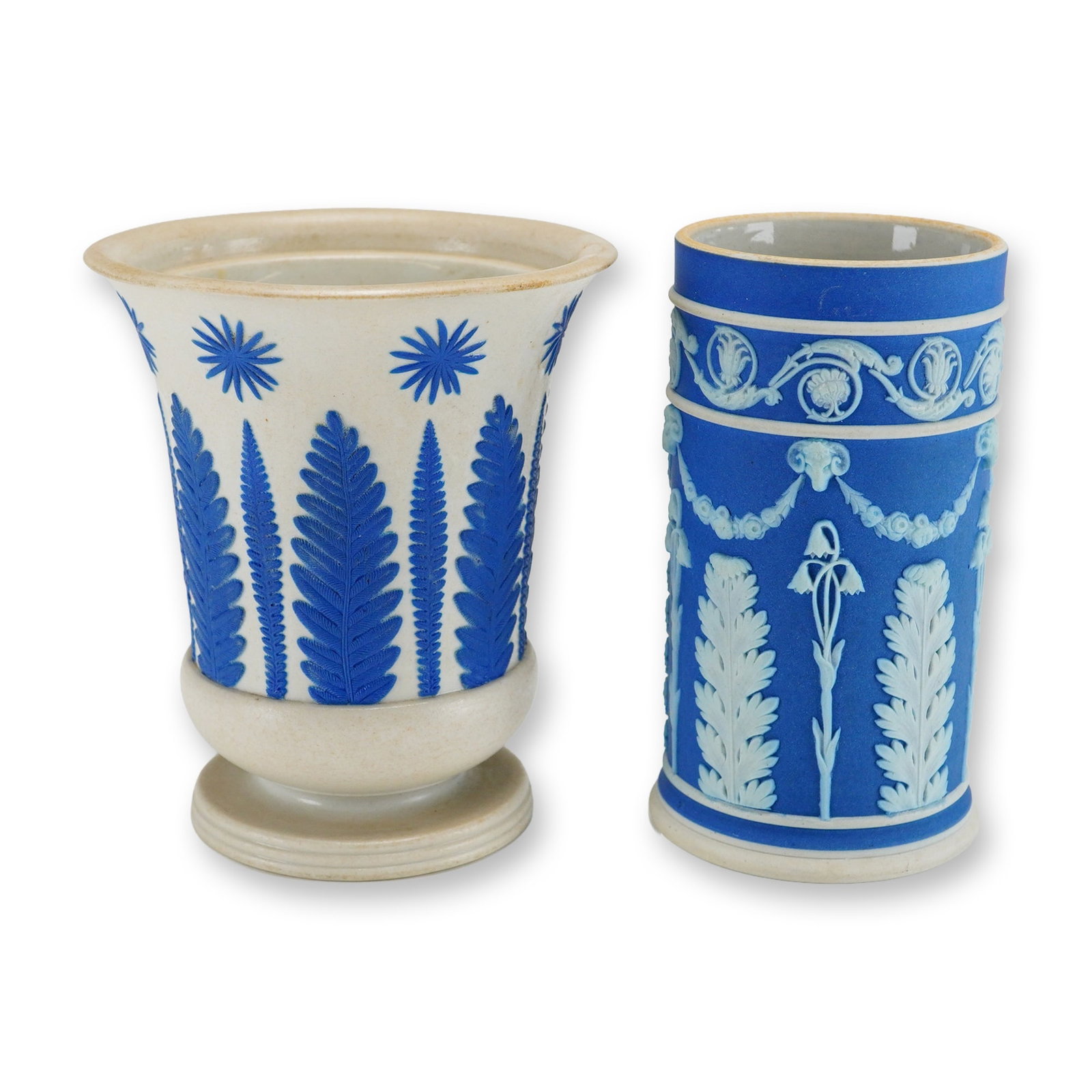 2pc Wedgwood Jasperware Vases: This lot consists of two distinct pieces of Wedgwood jasperware stoneware. The first is a flared, footed vase featuring a cream body with applied blue sprigged relief decoration of stylized sunbursts 