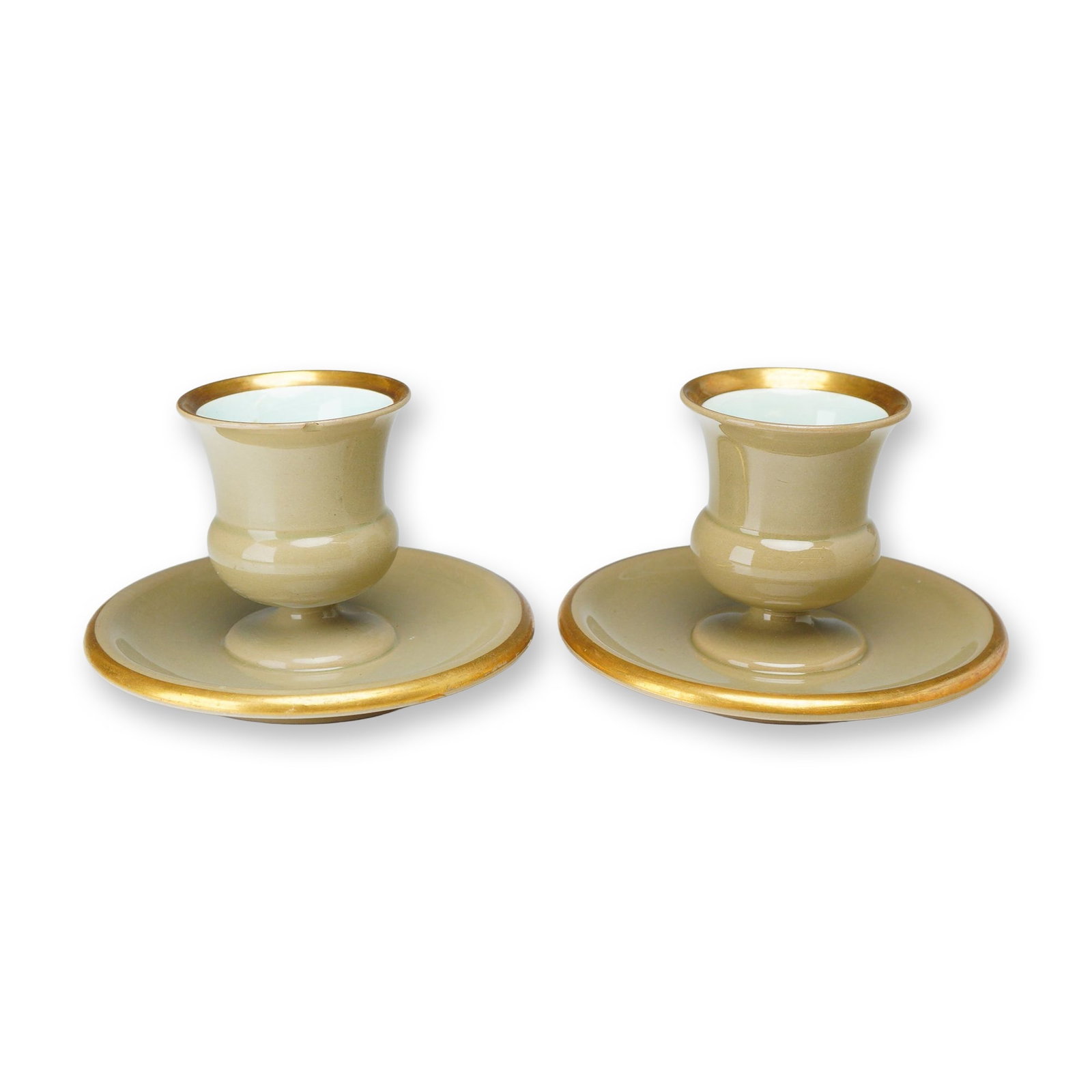 A Pair of Wedgwood Drabware and Gilt Ceramic Candleholders: A pair of glazed earthenware candleholders manufactured by Wedgwood. Each piece features a flared, pedestal-form candle cup integrated with a wide, flat saucer base. The exterior and saucer surfaces a