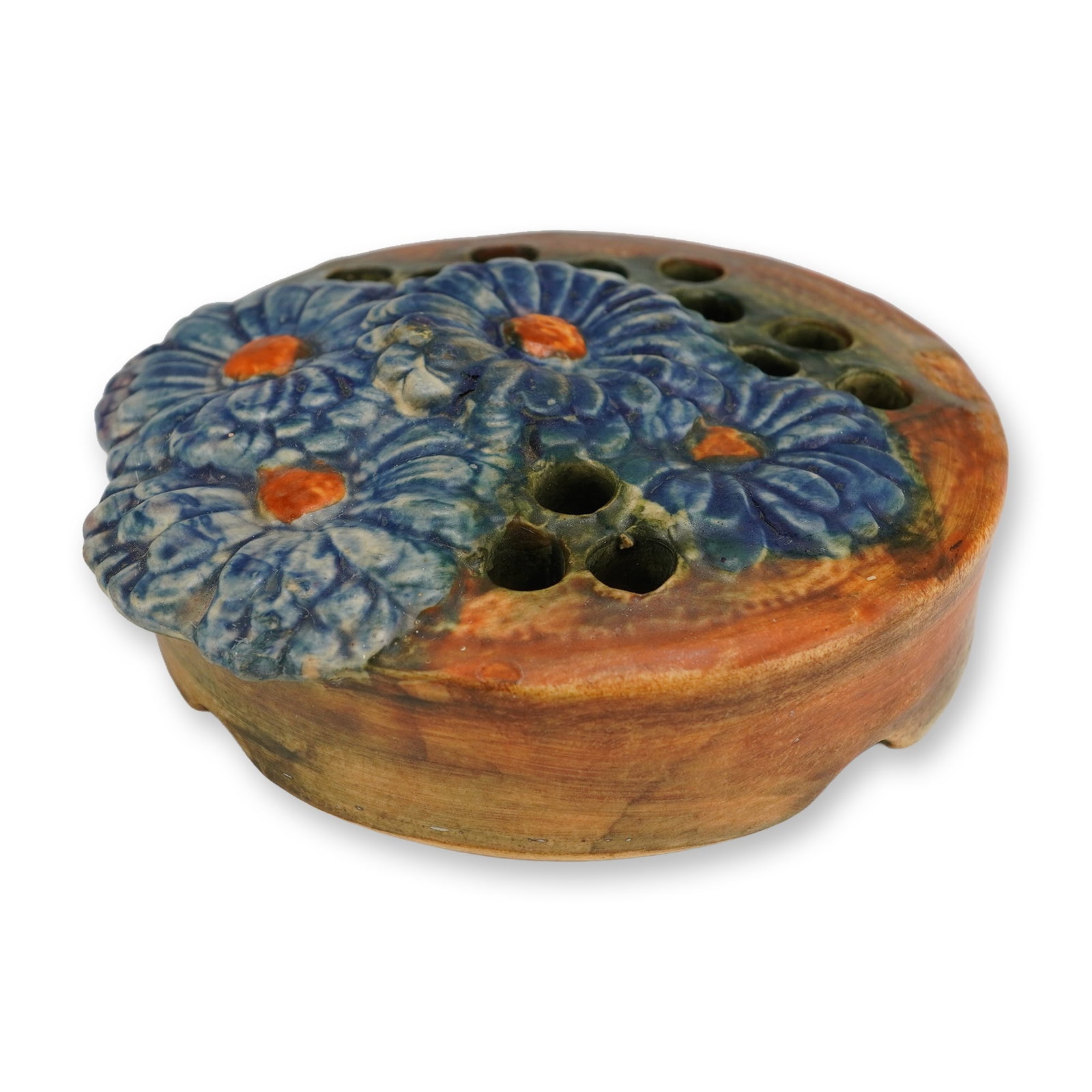 Weller Pottery Muskota Blue Daisy Flower Frog: A vintage Weller Pottery Muskota Blue Daisy flower frog of circular ceramic form. The piece features relief-molded blue flowers with bright orange centers, finished in a mottled glaze of brown,