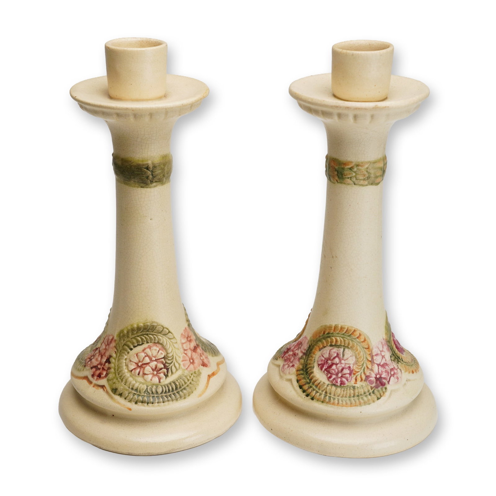 Pair of Weller Pottery Creamware Candleholders, Roma: Each piece features a tapered column rising from a flared circular base, finished in a characteristic matte cream glaze. The decoration consists of polychrome relief-molded accents, including a styliz