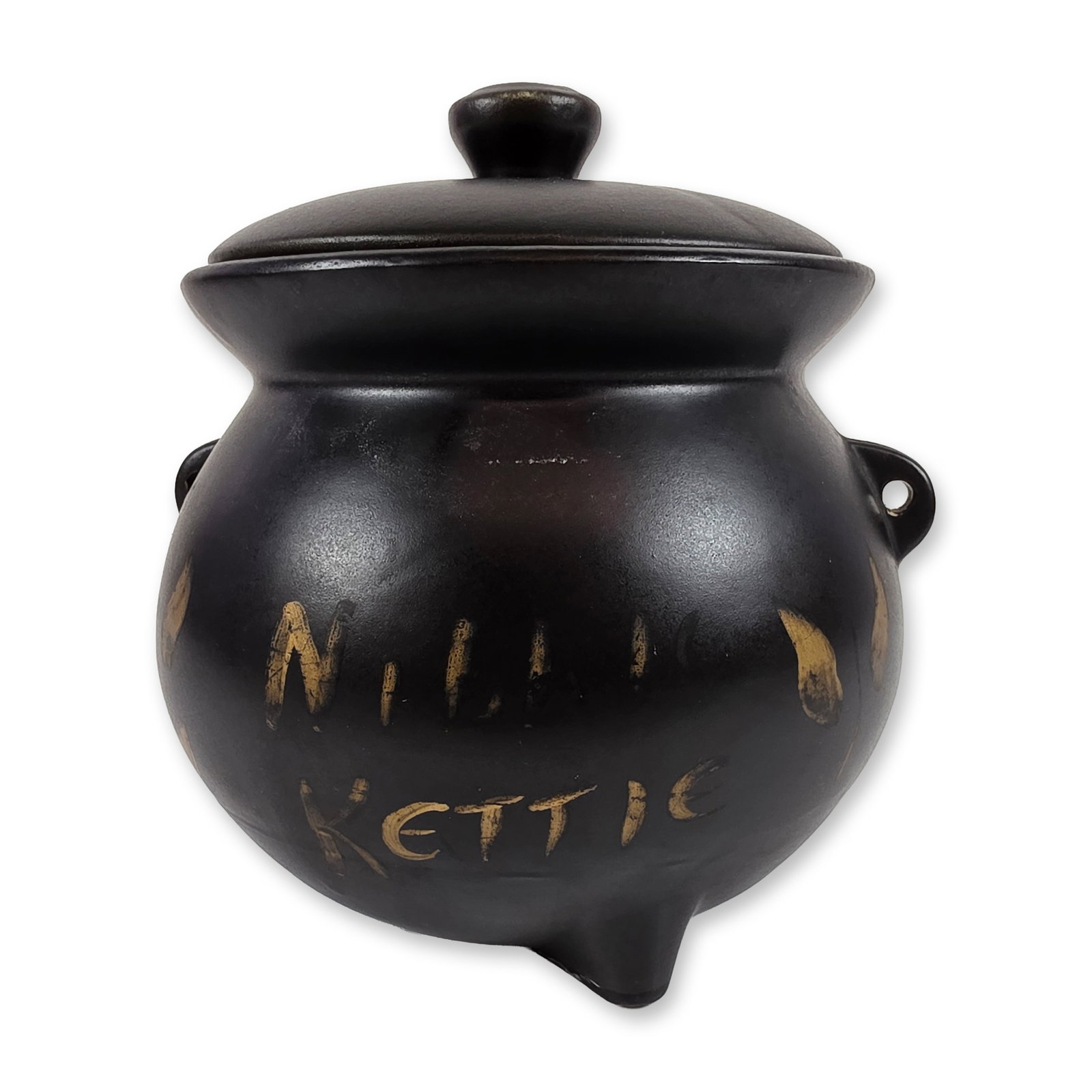 McCoy Ceramic Witches Kettle: The vessel is finished in a matte black glaze and features a globular body set on three tripod feet with a vestigial spout. Two pierced lug handles are located at the rim, though the wire bail is