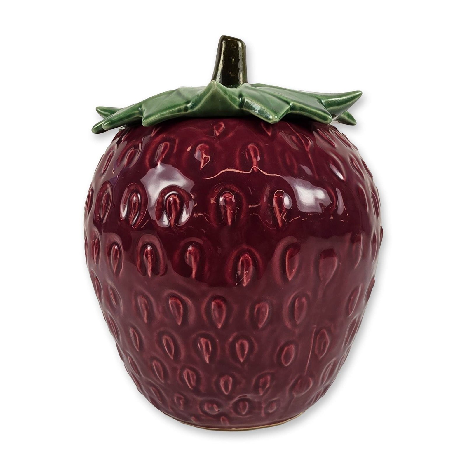 McCoy Ceramic Strawberry Cookie Jar: Modeled in the form of a large strawberry. The piece features a bulbous body with a molded textured surface depicting recessed seed impressions, finished in a high-gloss deep burgundy glaze. The match