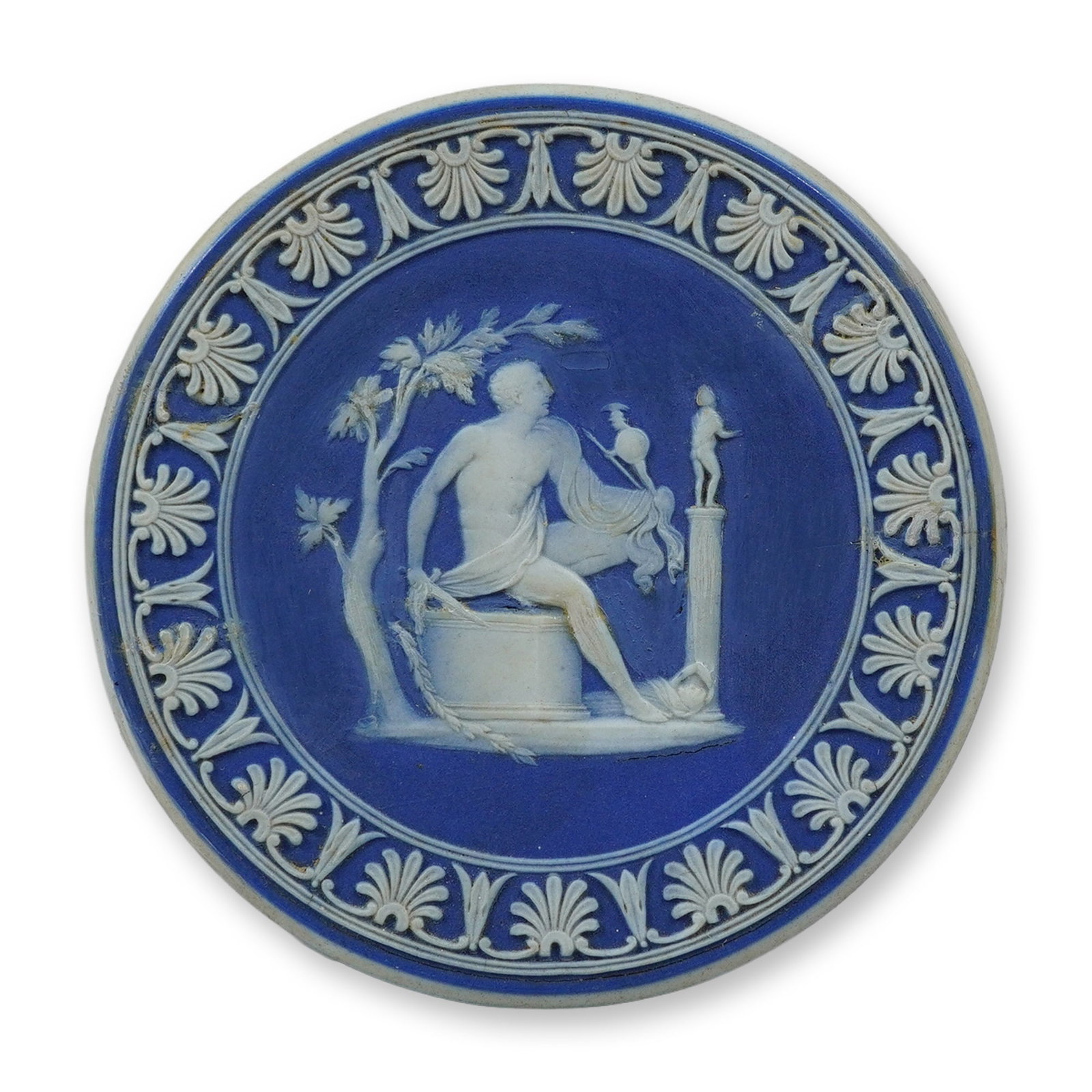 Wedgwood Solid Blue Jasperware Circular Medallion with Classical Relief: This circular stoneware medallion is a fine example of Wedgwood solid blue jasperware. The piece features a central scene in applied white jasper relief, depicting a seated male figure in classical dr