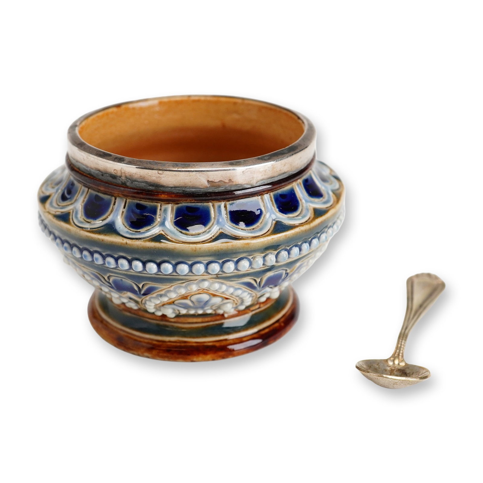 Doulton Lambeth Stoneware Salt Cellar with EPNS Spoon: A small bowl in blue, white, and brown tones, decorated with an Art Nouveau floral motif and accented by white beaded relief detailing. The piece features a sterling silver rim, and silver-plated (EPN