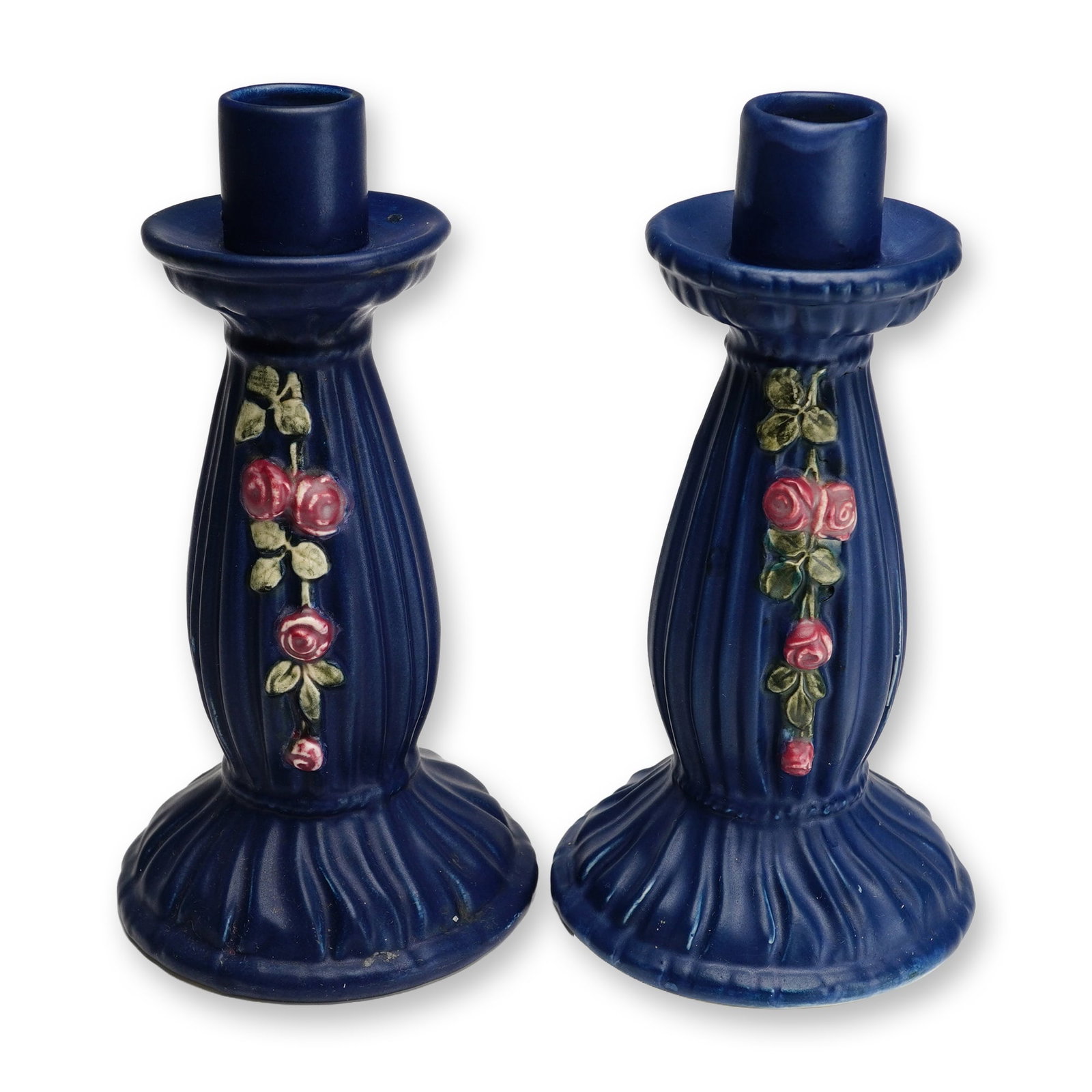 Pair of Weller Pottery Matte Candleholders, Blue Drapery: A pair of American art pottery candlesticks produced by Weller Pottery of Zanesville, Ohio, from the Blue Drapery line, circa 1915. Each molded ceramic piece features a deep matte blue glaze with a fl
