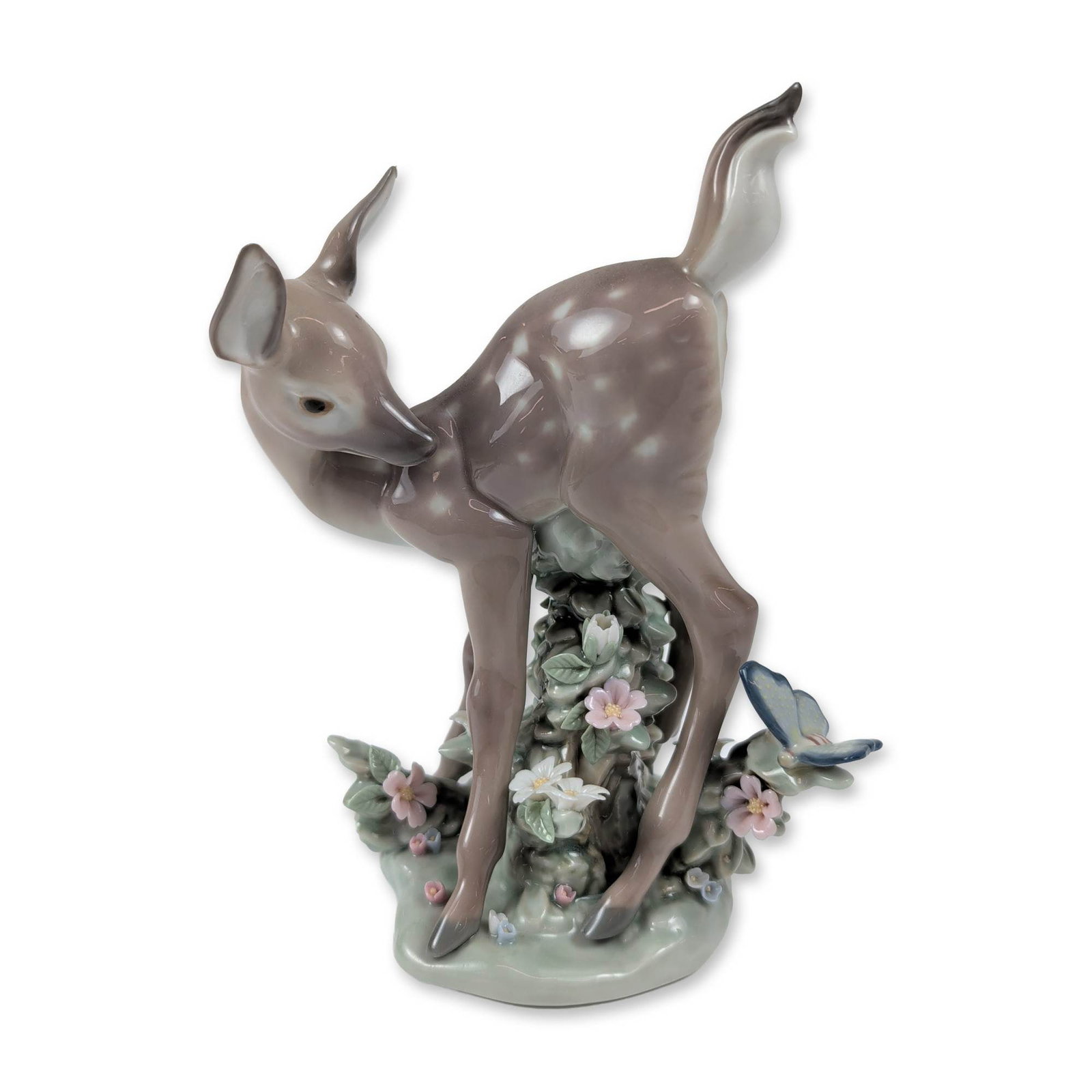 Lladro Glazed Porcelain Fawn Figurine, Hi There! 01005672: Model number 5672, titled Hi There!, shows a young spotted fawn in a lively pose, glancing back over its hindquarters. A blue butterfly rests on a cluster of pink and white flowers atop a mossy-green 