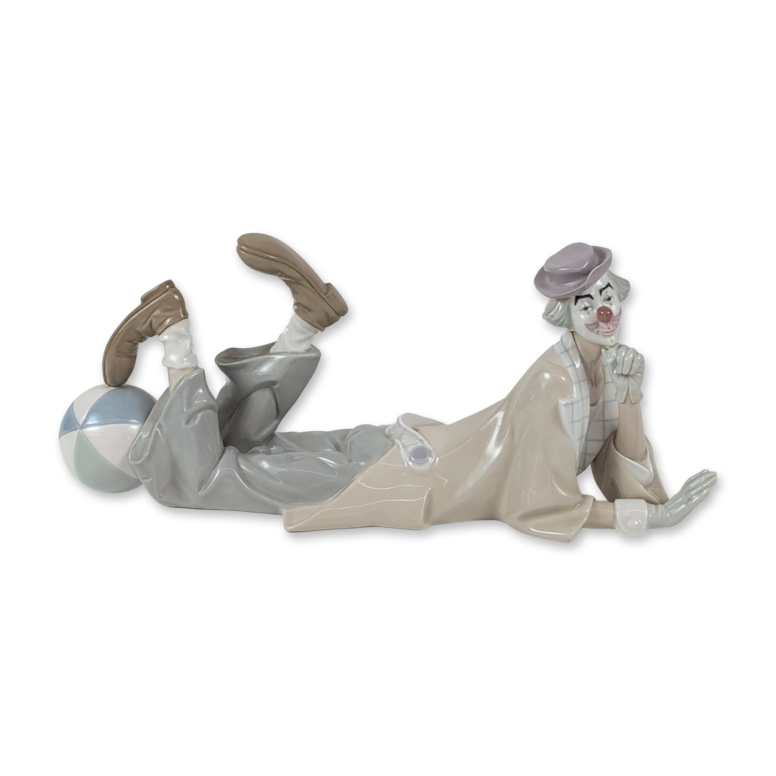Lladro Porcelain Figurine, Clown 1004618: Glazed porcelain figure depicting a reclining clown resting his head on one hand with a beach ball positioned under his bent legs, wearing a tan overcoat, checkered lapels, and lavender hat. Hand-pain