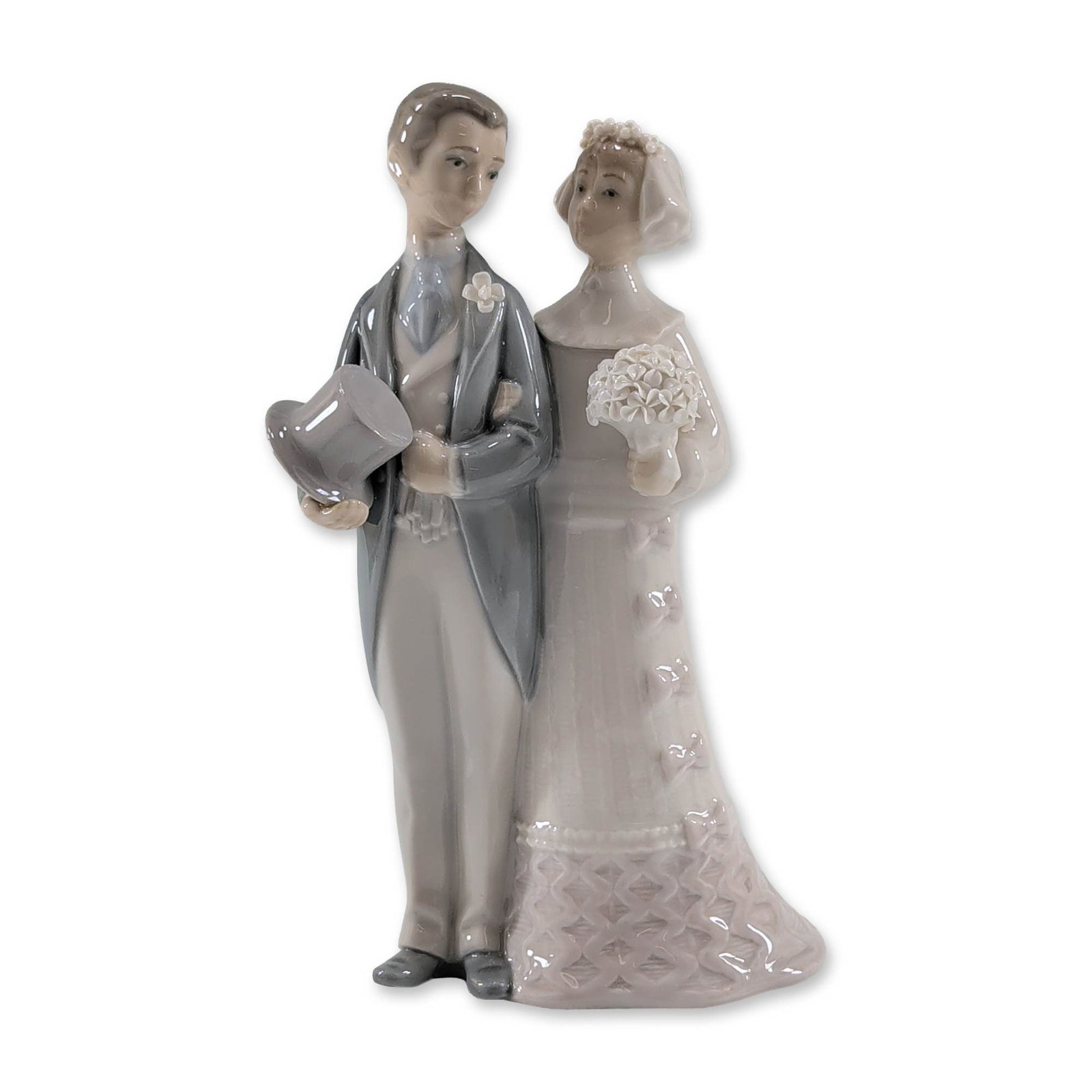 Lladro Glazed Porcelain Wedding Couple Figurine 1004808: Lladro (Spanish, 20th century). Wedding couple figurine in polychrome glazed porcelain, featuring a standing bride and groom. The groom is depicted in a grey tuxedo with a white lapel flower, holding 