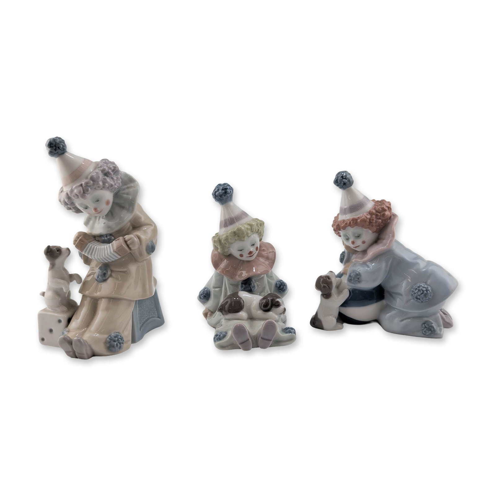Three Lladro Porcelain Pierrot Figurines: Lladro (Spanish, 20th century). Group of three glazed porcelain Pierrot figurines, featuring clowns in various poses accompanied by small dogs. The collection includes a seated figure with a puppy on 