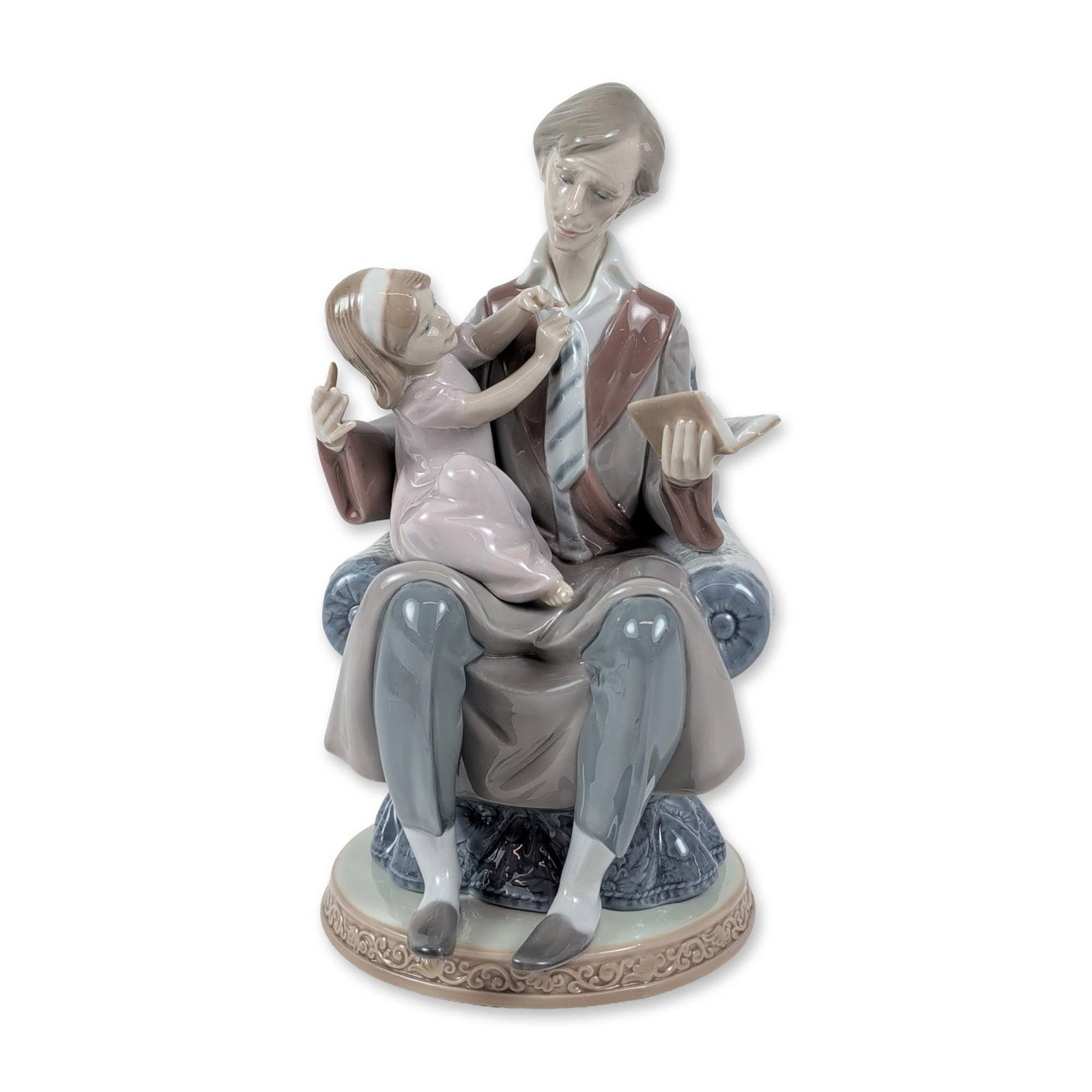 Lladro Porcelain Figurine, Daddy's Girl 1005584: Lladro Spanish glazed porcelain figurine titled Daddy's Girl, model number 5584, designed by Juan Huerta. The scene depicts a seated man in a grey robe and striped tie in a blue floral-patterned armch