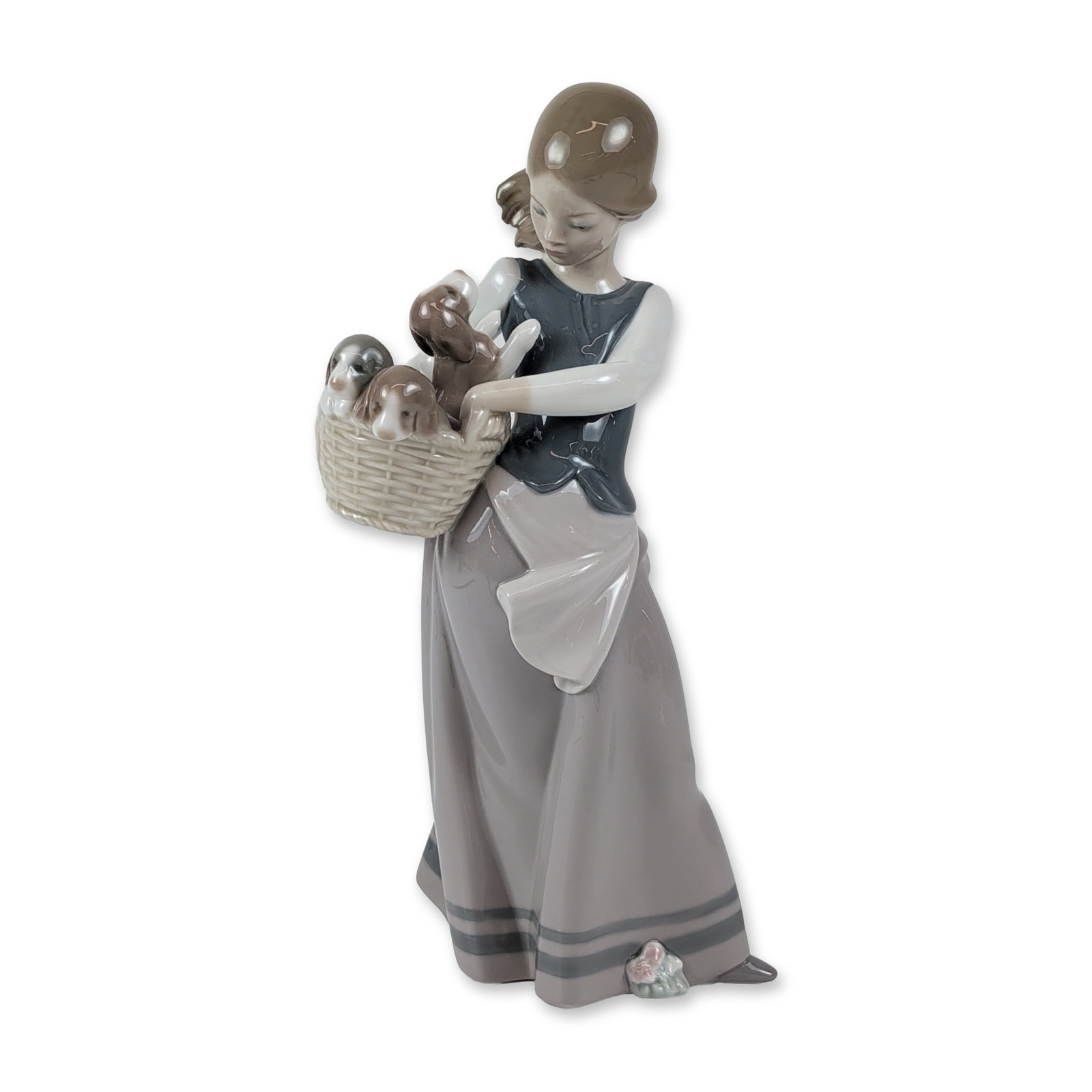 Lladro Porcelain Figurine, Girl with Puppies 1001311: Lladro glazed porcelain figurine model number 1311. The figure depicts a young girl in a long grey skirt with blue stripes, a dark blue bodice, and a white apron, supporting a large wicker basket cont