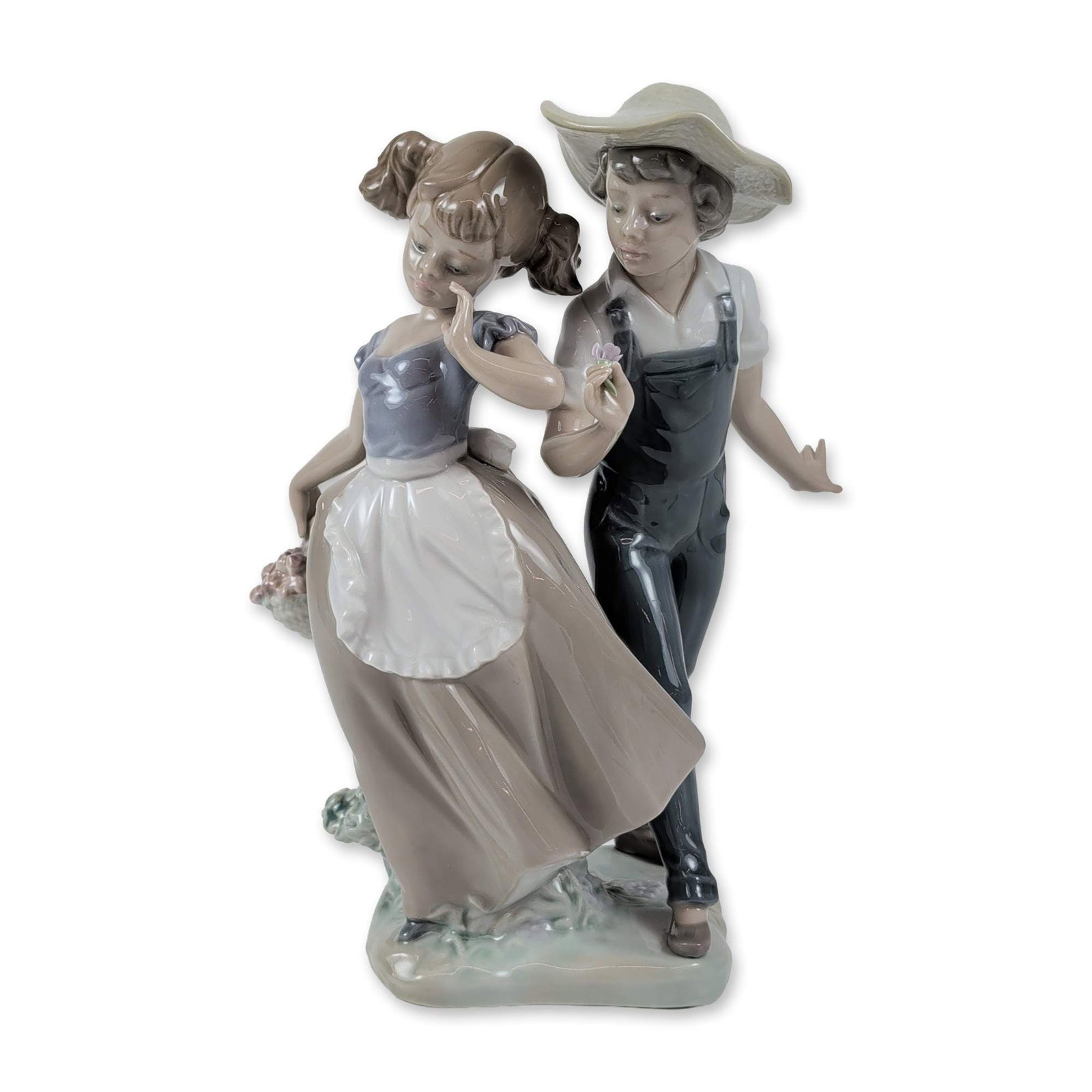 Lladro Porcelain Figurine, Love In Bloom 1005292: Lladro glazed porcelain figurine titled Love in Bloom, number 5292. The piece depicts a young boy dressed in dark-colored overalls and a wide-brimmed straw hat standing alongside a young girl in a blu