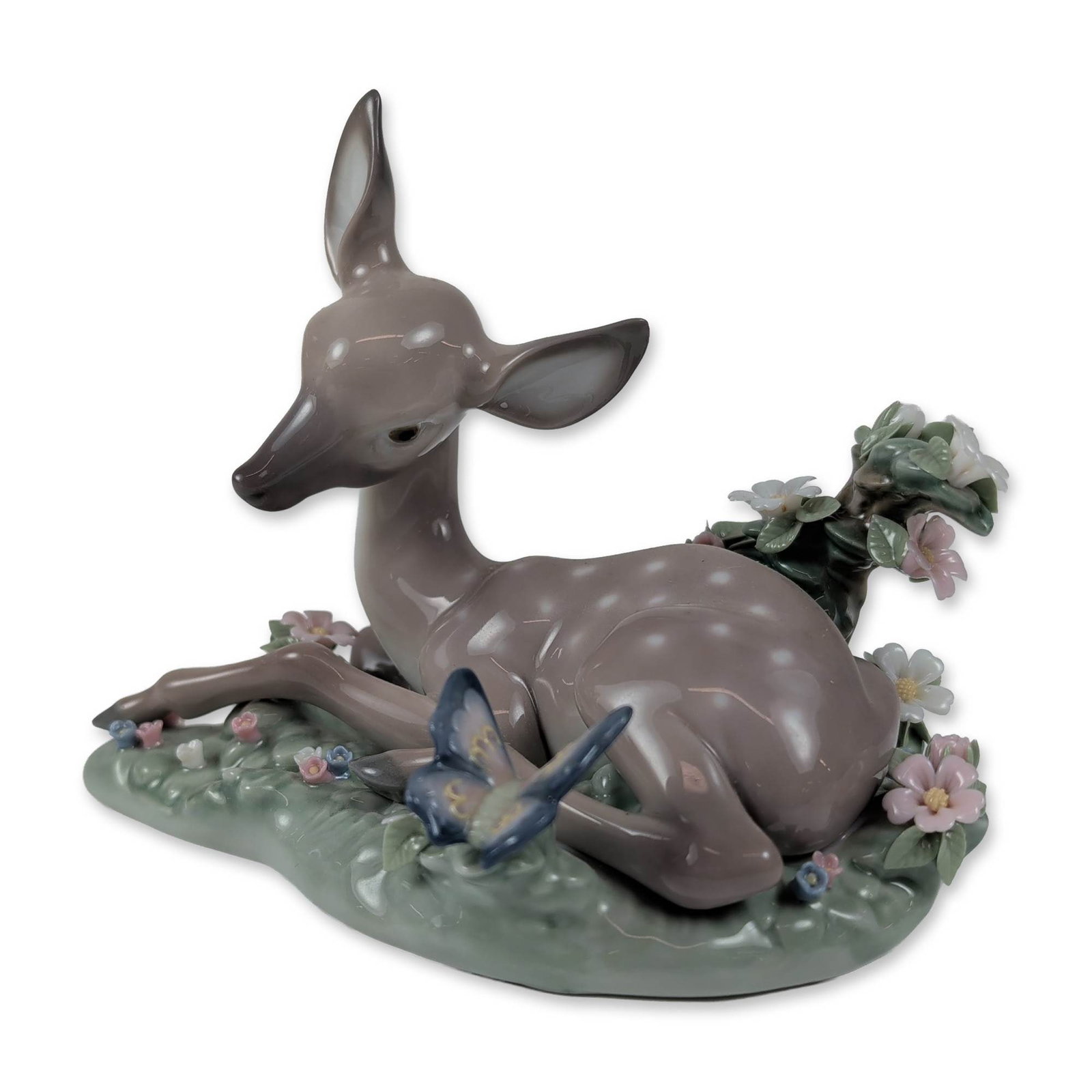 Lladro Spanish Porcelain A Quiet Moment Figurine 01005673: Model number 5673, crafted by Juan Huerta, features a glossy finish on a charming scene of a seated fawn watching a blue butterfly resting on a cluster of pastel-colored flowers. The underside of the 