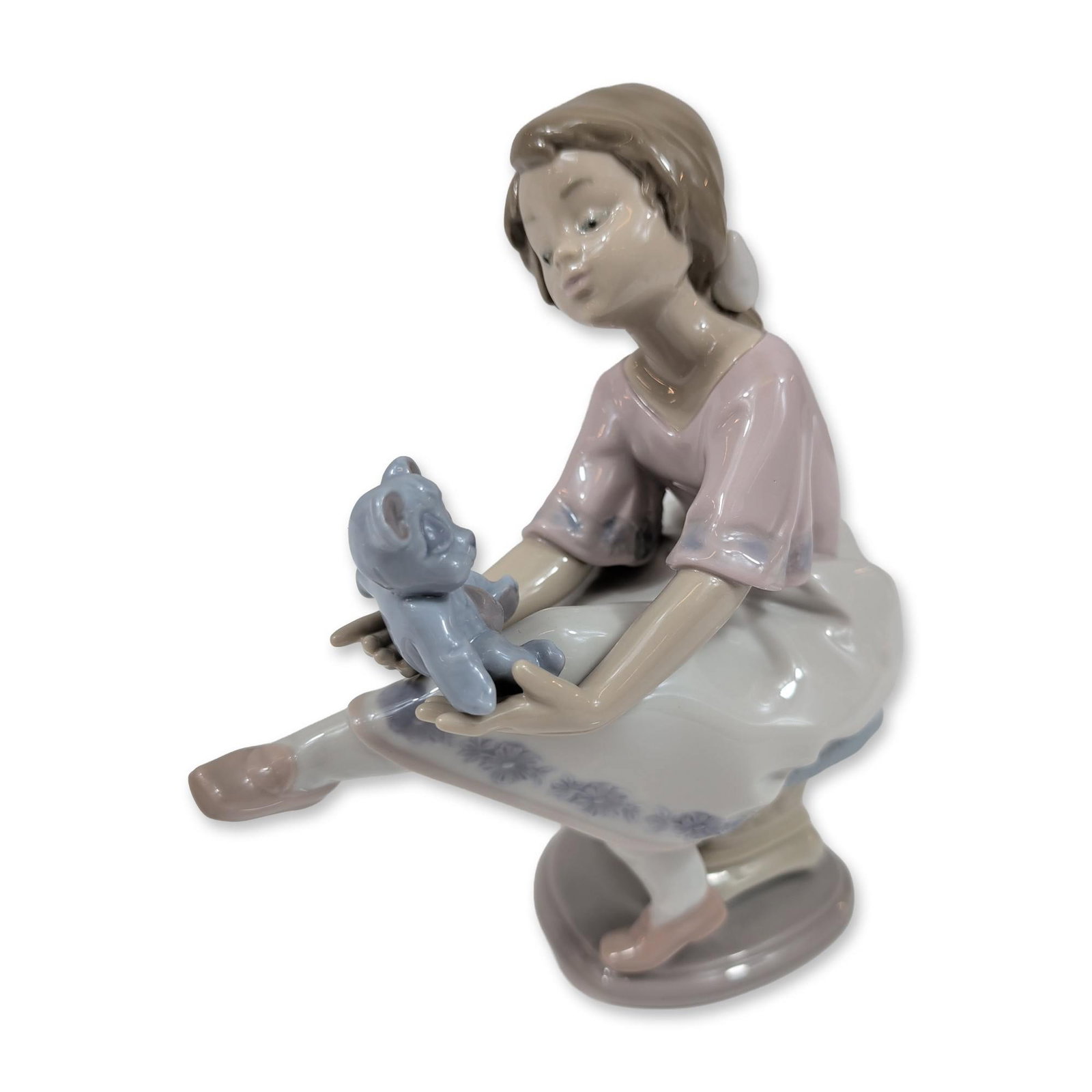 Lladro Porcelain Best Friend Figurine 7620: Lladro (Spain). Best Friend glazed porcelain figurine, model number 7620. The figure depicts a young girl seated on a textured pedestal, leaning forward to look at a small blue teddy bear held in her 