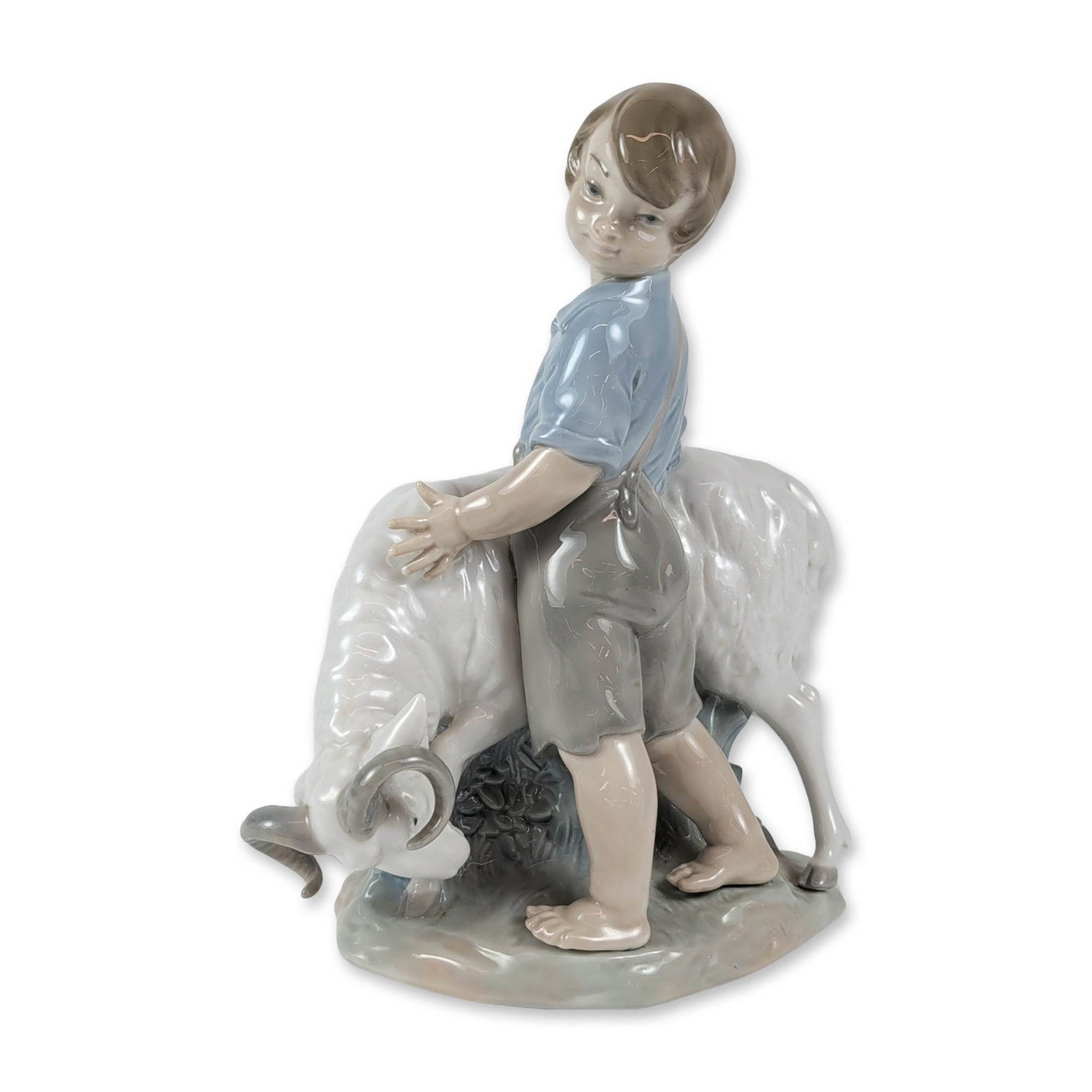 Nao by Lladro Porcelain Boy with Ram Figurine, I'm Not Moving: Nao by Lladro, a Spanish creation, is a glazed porcelain figurine showing a barefoot young boy in a blue short-sleeved shirt and grey overalls leaning over a white ram with big curled horns. It rests 