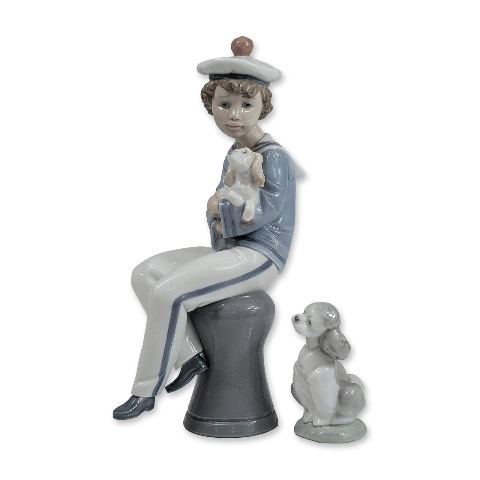 2pc Lladro Figurines, Seaside Companions and A Friend for Life: Lladro, Spain. Two glazed porcelain figurines featuring nautical and canine subjects. The first figure, titled Seaside Companions (model 6196), depicts a young boy in a sailor uniform with a red pom-p