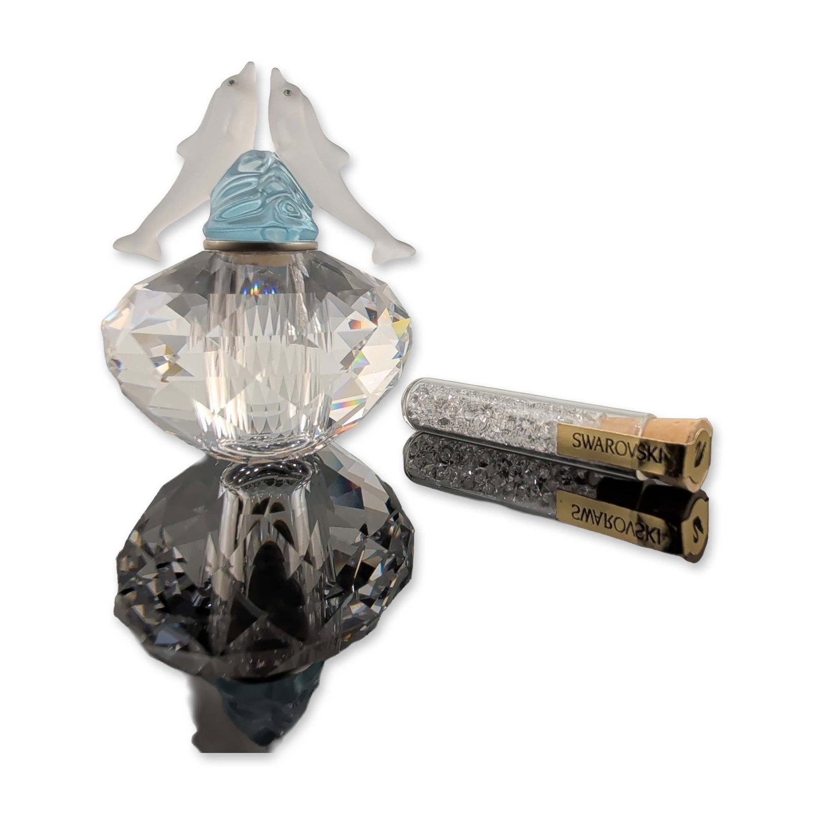 Swarovski Crystal Dolphin Flacon Bottle: Flacon in faceted clear and frosted crystal, featuring a figural stopper with two dolphins leaping over a translucent blue crystal wave. The lot includes a small glass vial containing loose clear and 