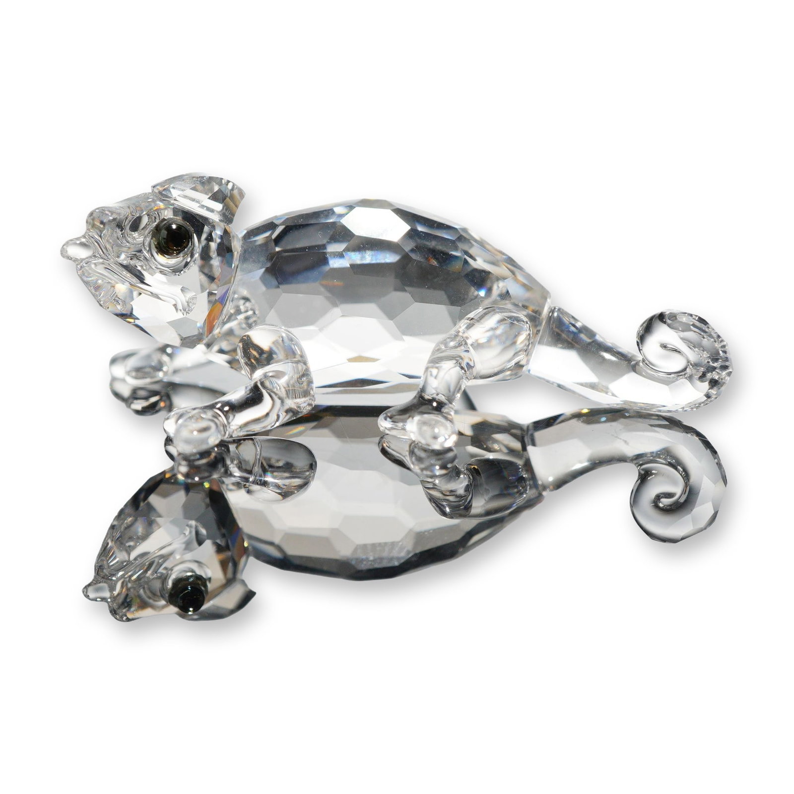 Swarovski Crystal Chameleon Figurine: This piece features a faceted clear crystal body with a smooth molded crystal head, splayed legs, and a curled tail. The eyes are accented with small, inset dark crystals. Features an etched Swarovski