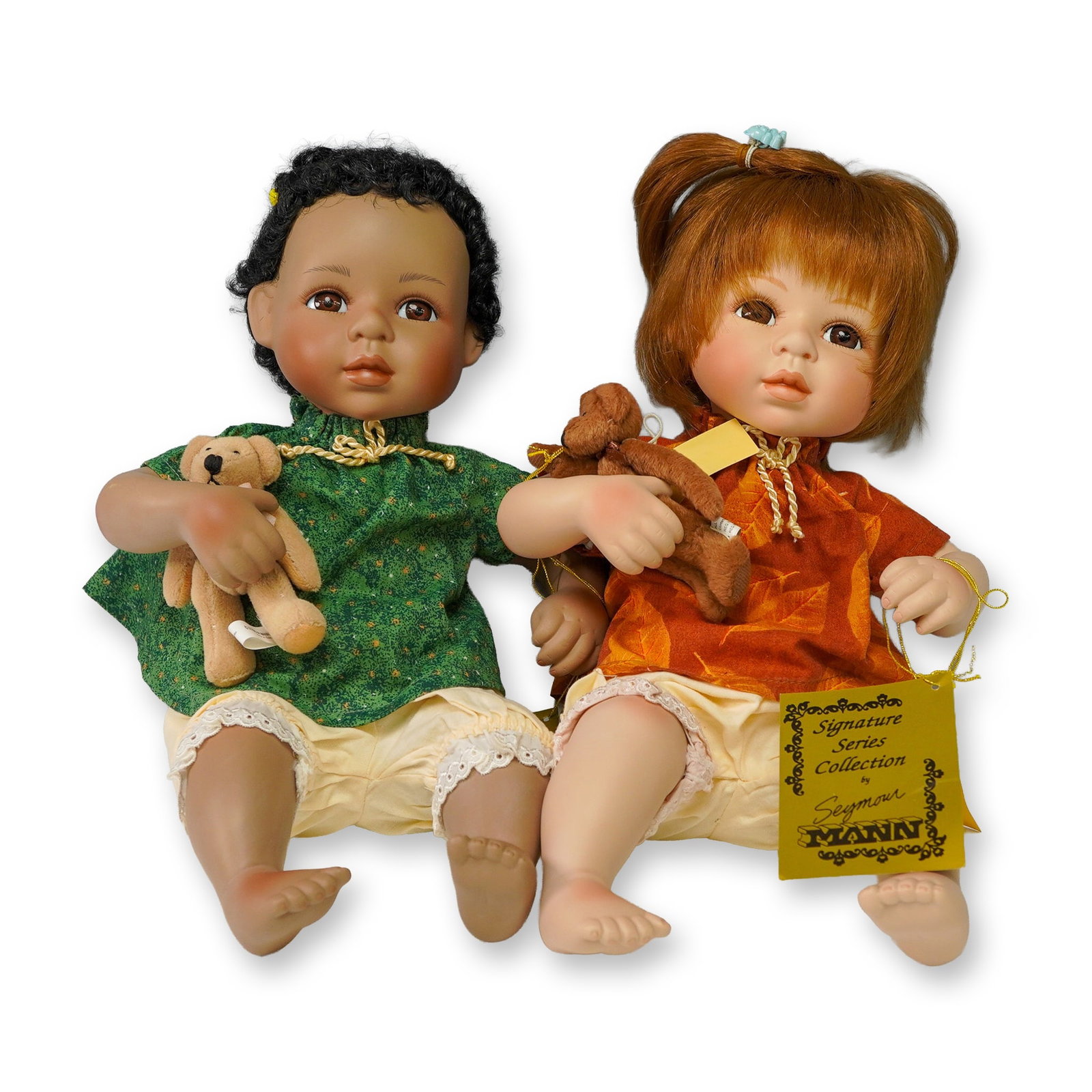 Seymour Mann Signature Series, Baby Dolls Set: This charming set features two Seymour Mann Signature Series porcelain baby dolls, each measuring 13 inches tall. One baby has red hair styled in pigtails and wears a rust-orange tunic, while the othe