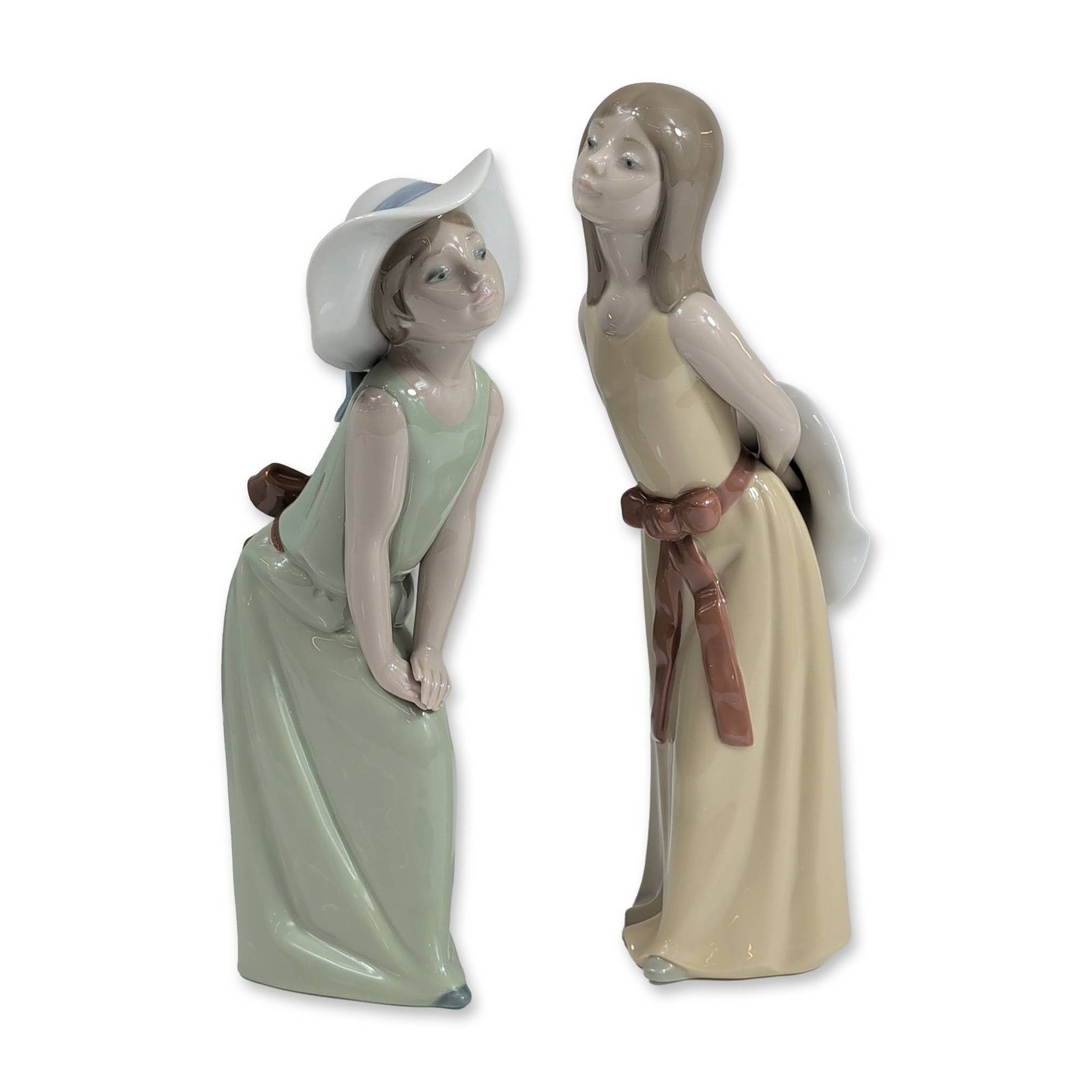 2pc Lladro Porcelain Figurines: Lladro, Valencia, Spain. Pair of glazed porcelain figurines featuring young women in pastoral attire. Model 5006, known as Naughty Girl with Straw Hat, depicts a figure in a light green floor-length g
