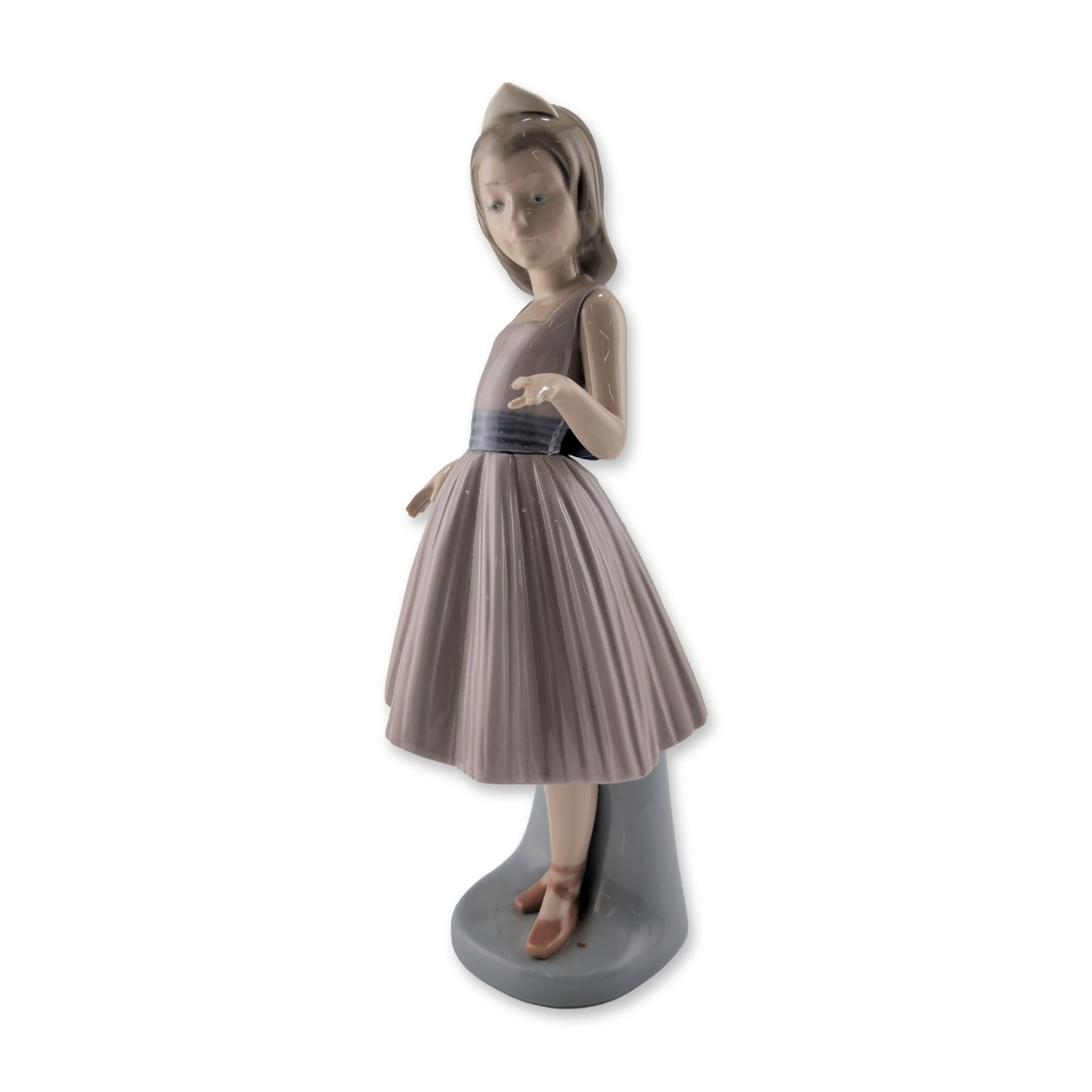 Lladro Glazed Porcelain Figurine, A Dancing Partner 01005093: Lladro, Spain. Glazed porcelain figurine depicting a young girl in a lavender-gray bodice and finely pleated skirt. The figure features a wide blue sash tied in a large bow at the reverse and a white 