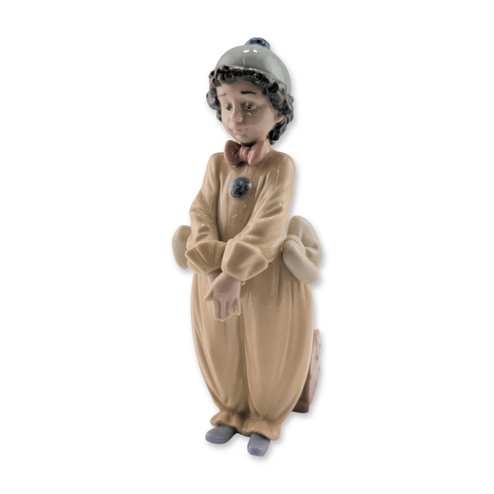 Lladro Porcelain Figurine, Pierrot in Love 01006258: Spanish manufacture, Lladro. A child clown figurine in glazed porcelain, titled Pierrot in Love. The figure depicts a pensive young boy in a tan jumpsuit with grey pom-poms, a ruffled collar with a pi