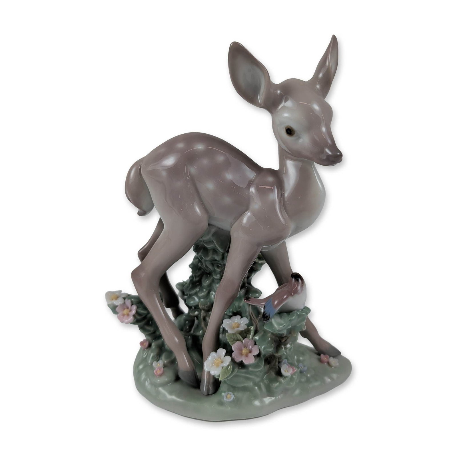 Lladro Glazed Porcelain Figurine Faun and a Friend 01005674: Model 5674, titled Faun and a Friend, shows a fawn glancing back at a bird perched on its hindquarters. The piece rests on a landscape base decorated with hand-applied pink and white flowers. On the u
