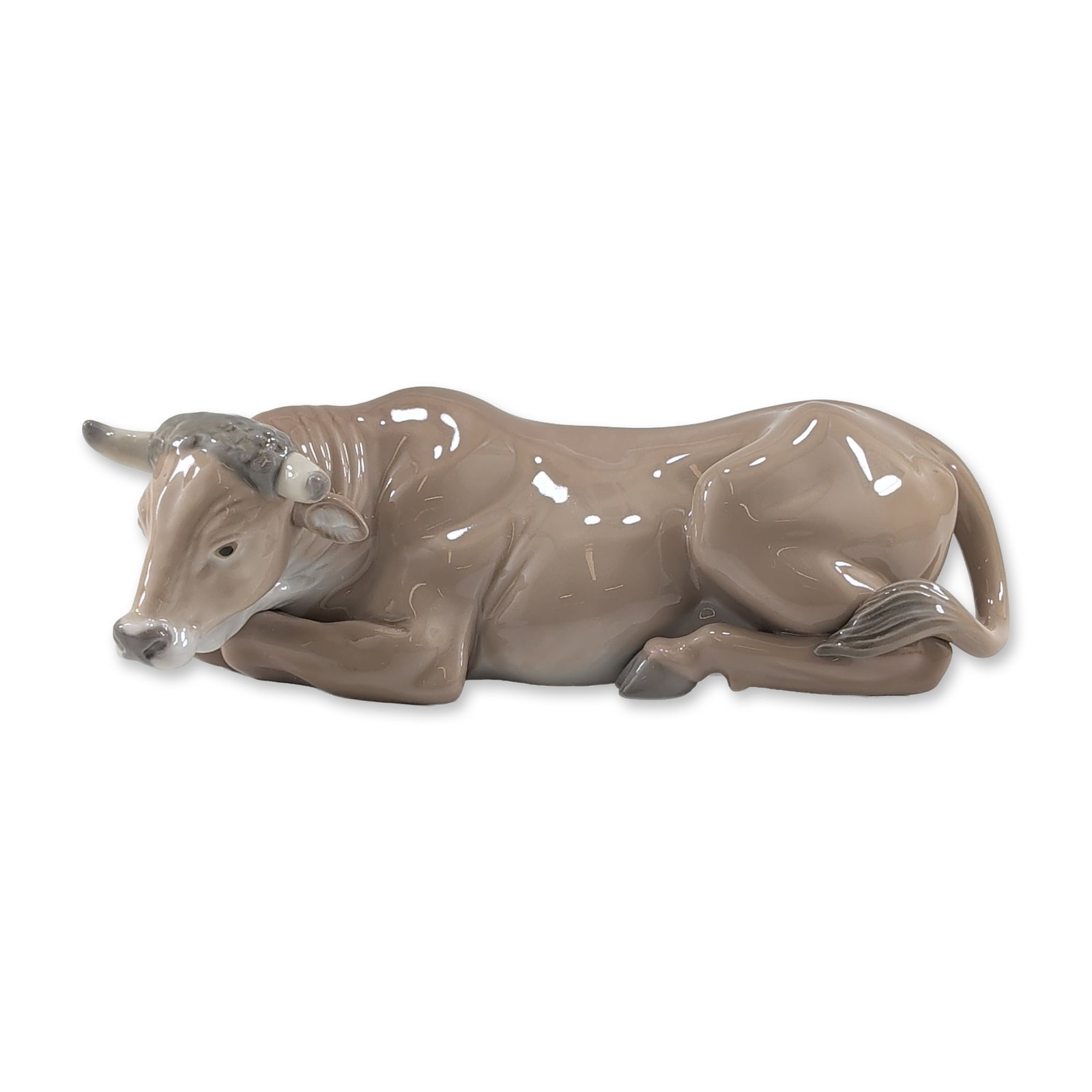 Lladro Spanish Porcelain Ox Figurine: Lladro, Spain. Ox figurine in glazed porcelain, featuring a recumbent form with a taupe-colored body and greyish accents to the head and horns. Finished in a uniform high-gloss glaze. The underside be
