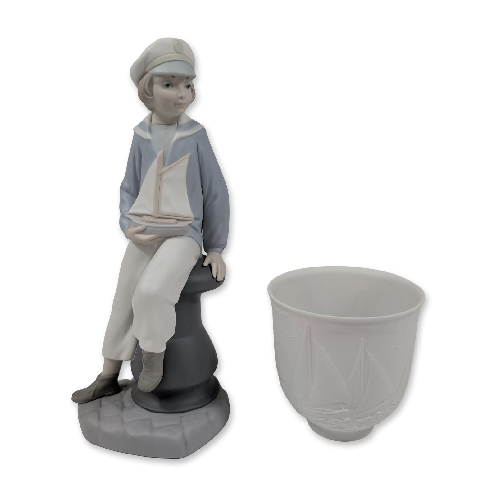 Lladro Porcelain Boy With Yacht and Vessel: Lladro, Spain. Two porcelain items including a Boy with Yacht figurine and a nautical-themed vessel. The figurine, model 4810, is executed in glazed and matte porcelain, depicting a young boy in a sai