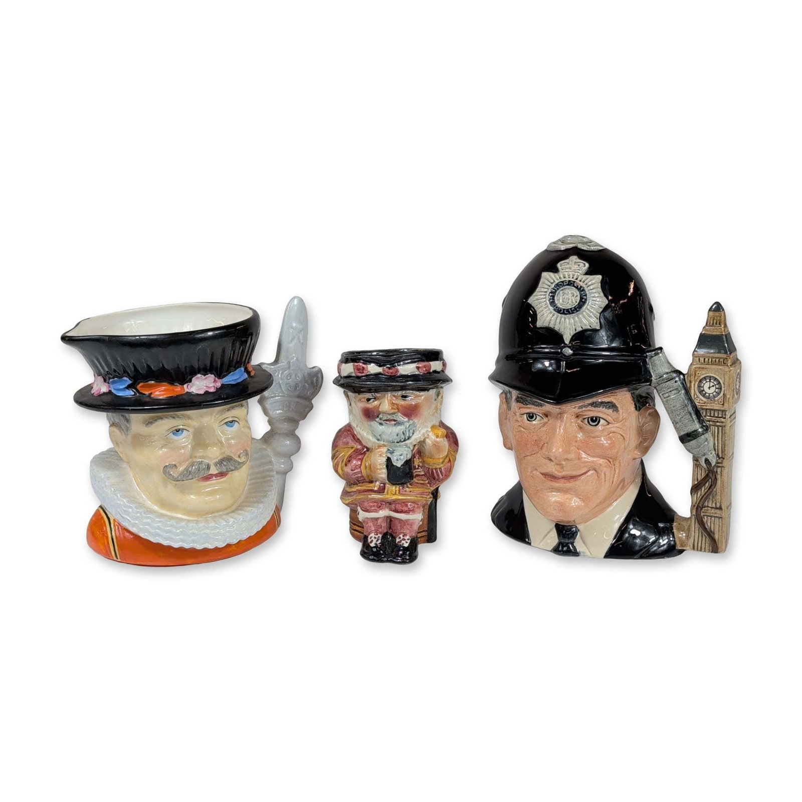 3pc Royal Doulton and Staffordshire Ceramic Character Jugs: Trio of English glazed ceramic character jugs depicting British cultural figures. The group includes a Royal Doulton large character jug titled The London Bobby, model D 6744, designed by Stanley Jame