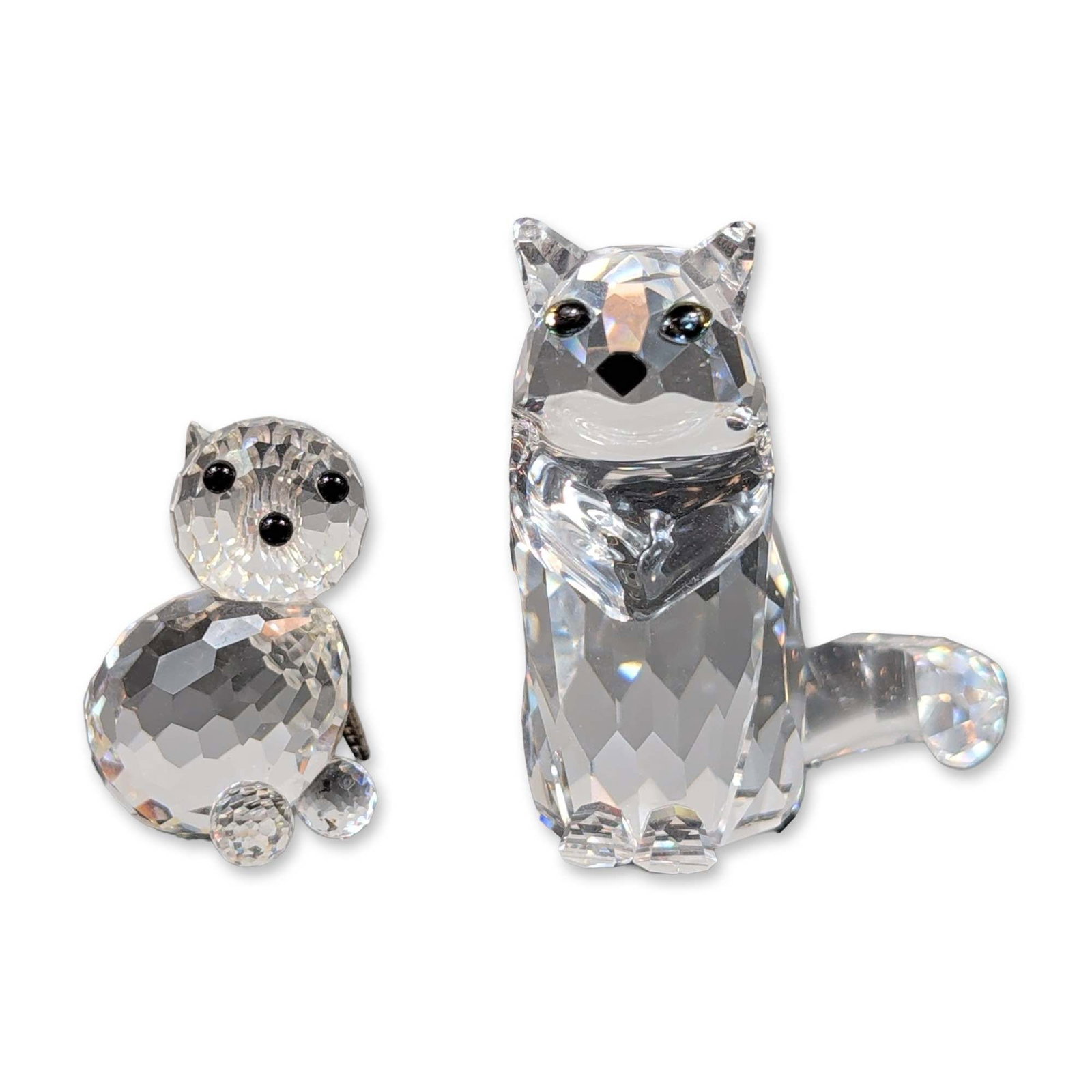 Two Swarovski Clear Crystal Cat Figurines: Swarovski figurines crafted in faceted clear lead crystal depict a larger cat and a kitten. The larger cat is seated, with polychrome eyes and a black nose, while the kitten sits with a silver-tone me
