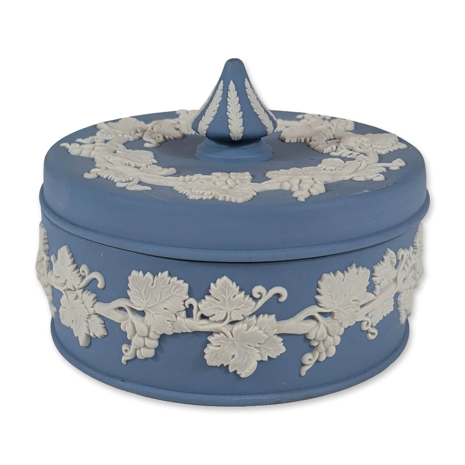 Wedgwood Blue Jasperware Grapevine Lidded Box: Wedgwood pale blue jasperware circular lidded box featuring white bas-relief grapevine decoration. The lid is detailed with a central foliate-ribbed finial and a surrounding grapevine wreath. The body