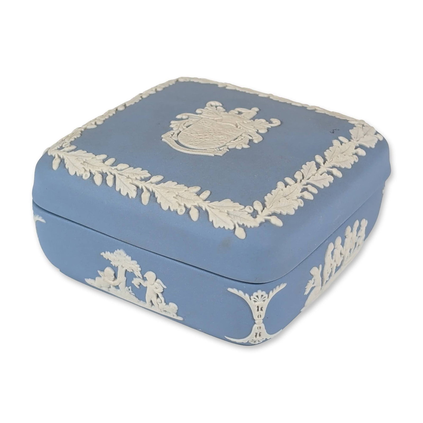Wedgwood English Blue Jasperware Trinket Box: Wedgwood. Square lidded trinket box in pale blue Jasperware, featuring a central heraldic coat of arms on the cover framed by an oak leaf and acorn border. The sides are adorned with white bas-relief 