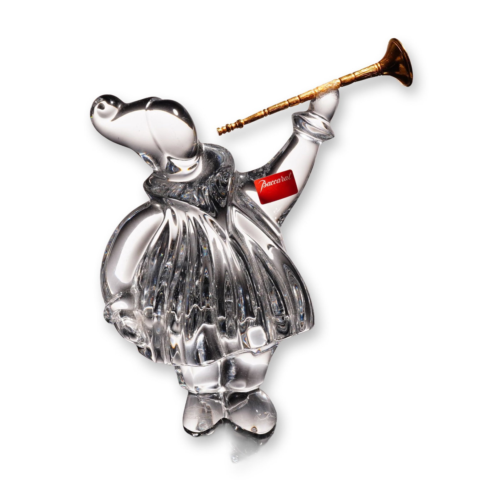 Baccarat by Jean Boggio Crystal Masquerade Trumpeter Figurine: The piece depicts a stylized anthropomorphic elephant, characterized as a trumpet angel, standing in a vertically ribbed garment with a ruffed collar. The figure holds a gold-toned metal trumpet to it