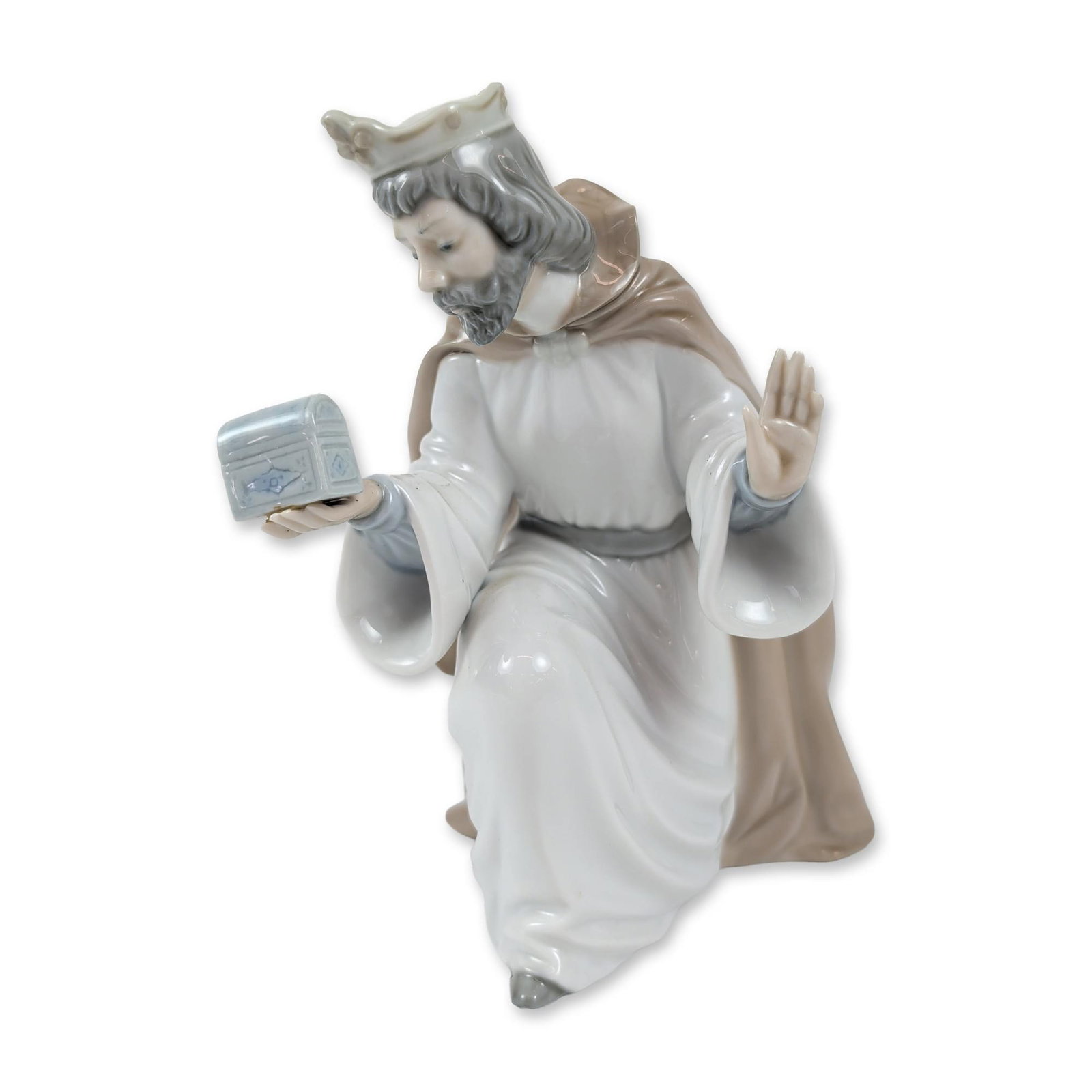NAO by Lladro King Melchior with Chest Porcelain Figurine: This porcelain figurine of King Melchior, part of a Nativity collection, was handcrafted in Spain. Depicted kneeling, he wears a crown and flowing robes in shades of white, tan, and pale blue. One han