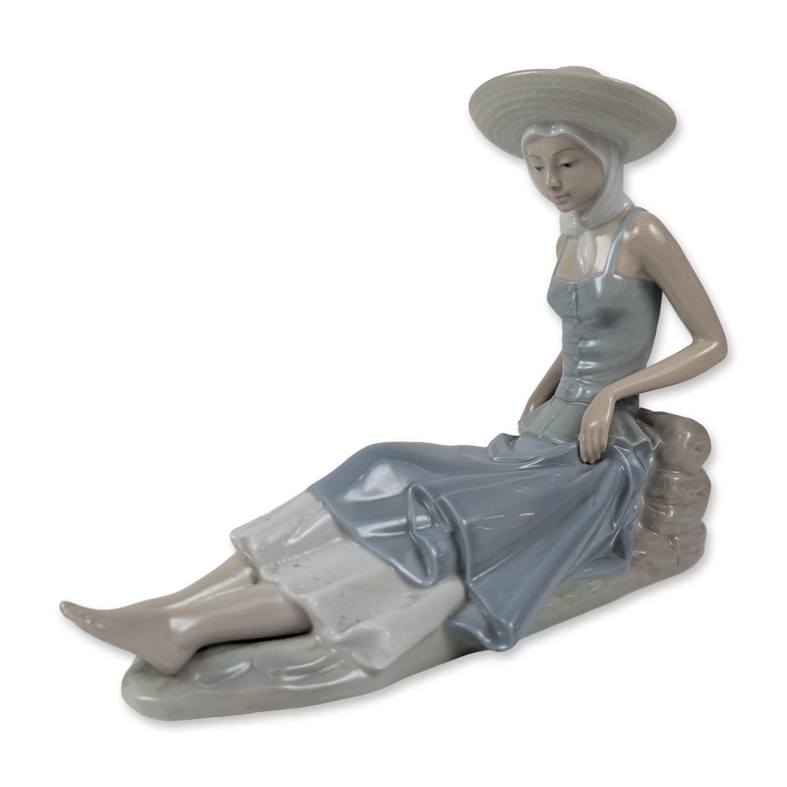 Nao by Lladro Porcelain Seated Woman Figurine: Large glazed porcelain figurine depicting a seated woman wearing a wide-brimmed sun hat with a chin strap, a sleeveless blue bodice, and a layered blue and white skirt. The figure is modeled resting a