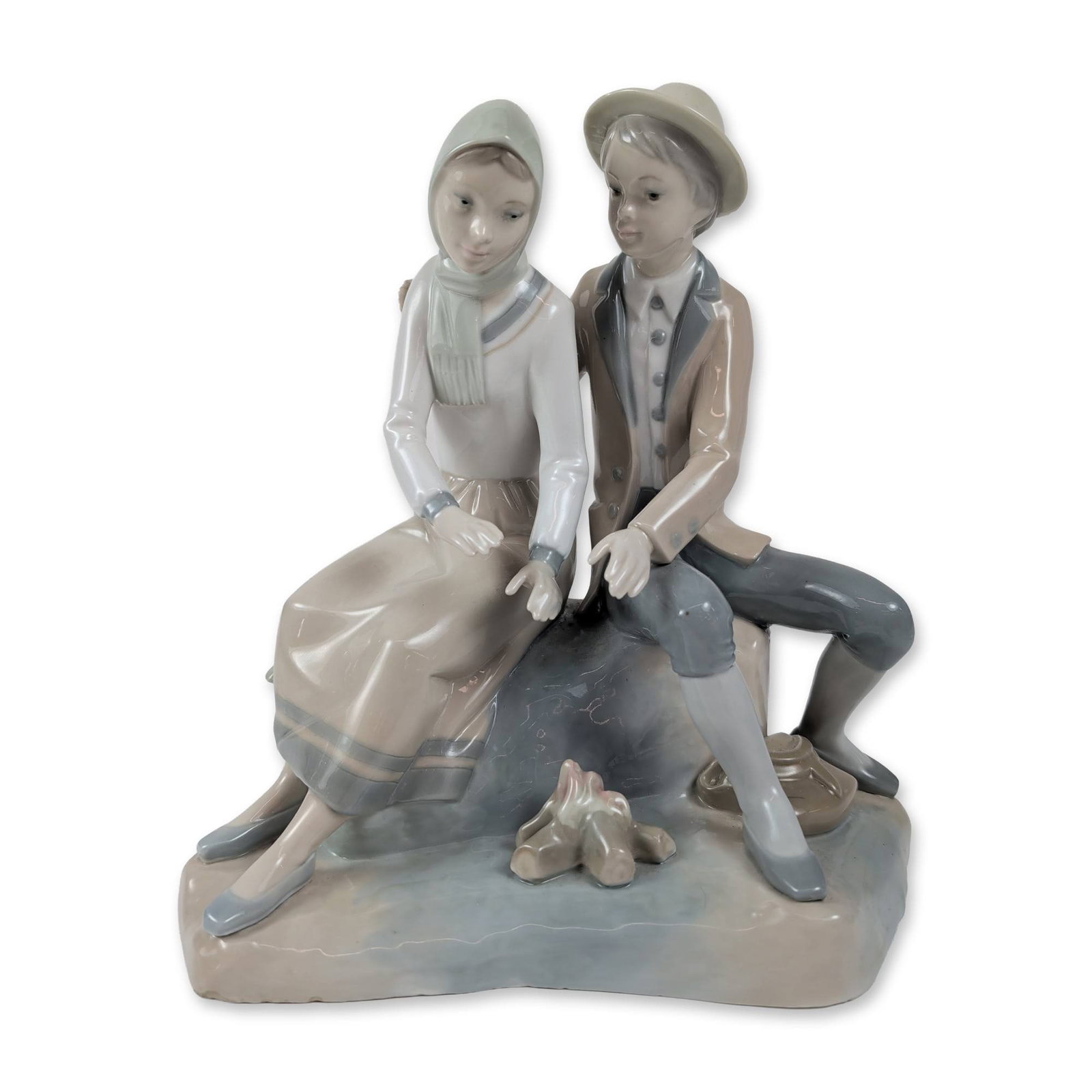 Zaphir Spanish Porcelain Couple Figurine: Zaphir, Spain. Porcelain figurine depicting a young couple in period attire seated on a rocky outcrop beside a campfire. The male figure is depicted in a brimmed hat and long coat, while the female fi