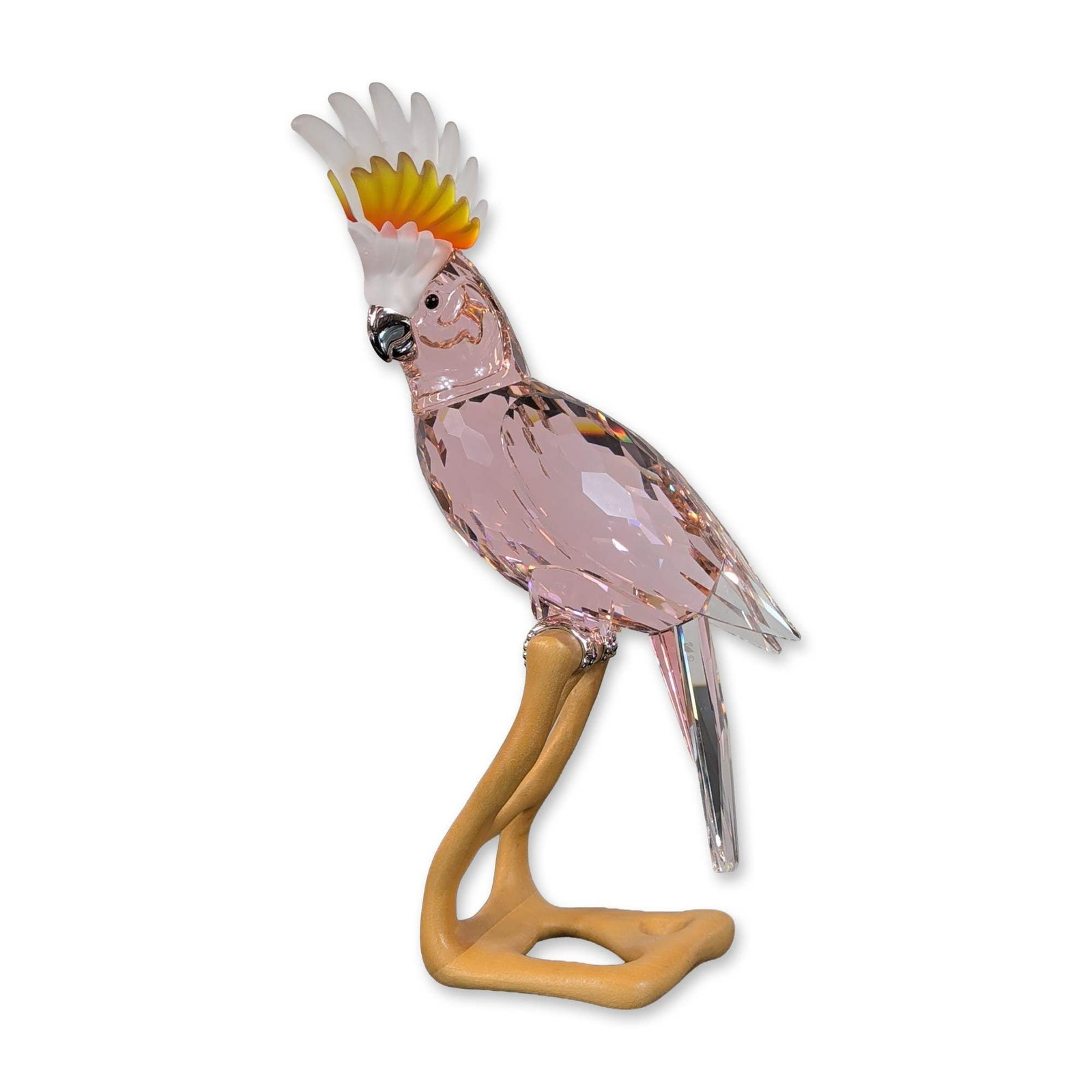 Swarovski Crystal Paradise Birds Figurine, Cockatoo: Swarovski Paradise series. Bird figurine in faceted pink and clear crystal, featuring a multi-tonal frosted crest and silver-tone metal beak and feet. The cockatoo is perched on a light-colored wooden