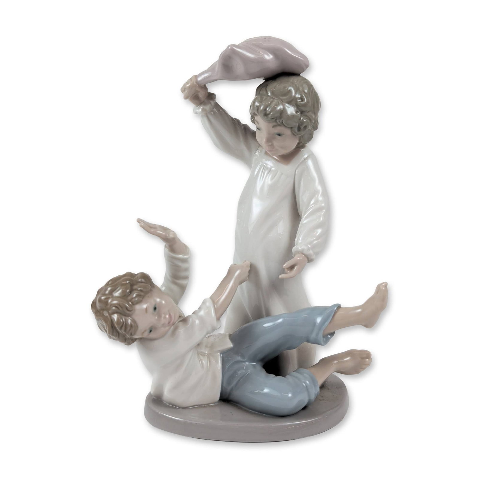 Nao by Lladro Porcelain Pillow Fight Figurine: Designed by sculptor Juan Huerta, the composition features two young boys in pajamas engaged in a playful pillow fight. One figure is depicted standing with a pillow raised, while the companion figure