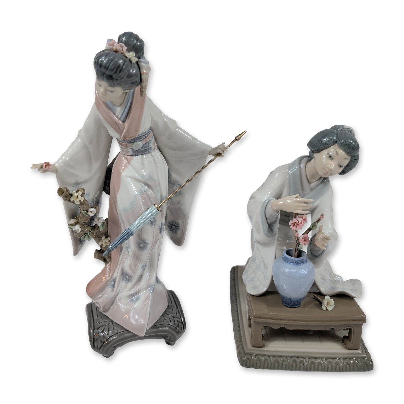 2pc Lladro Porcelain Figurines, Teruko and Mayumi.: Lladro, Spain. Pair of glazed porcelain figurines depicting Japanese women in traditional dress, featuring hand-applied floral elements. The standing figure, model number 1451, is depicted in a floral