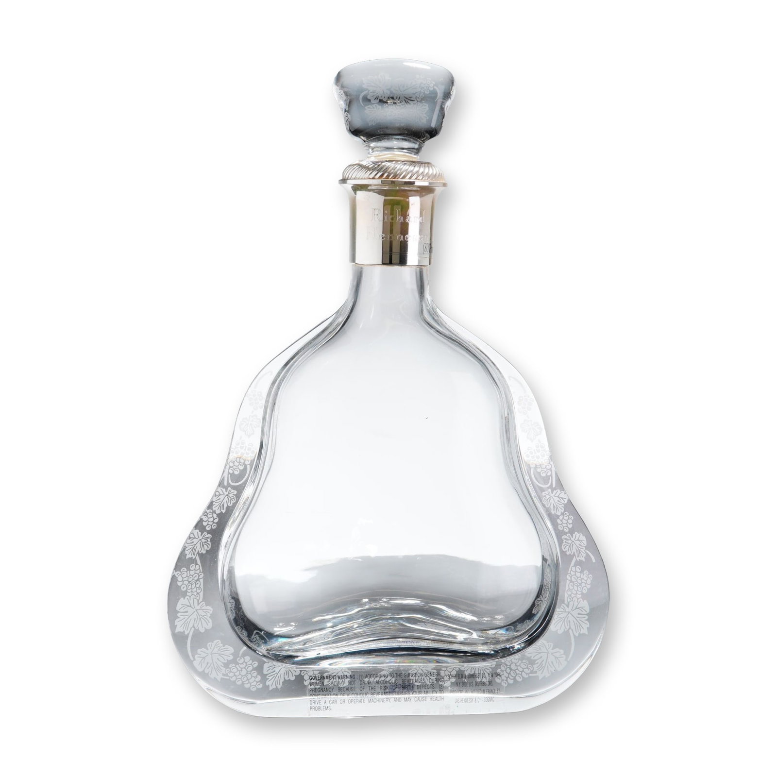 Baccarat Richard Hennessy Crystal Cognac Decanter: A French crystal cognac decanter crafted for Richard Hennessy, featuring a flattened pear-shaped body with a wide flared base and hand-etched grapevine and leaf motifs along the perimeter. The neck is