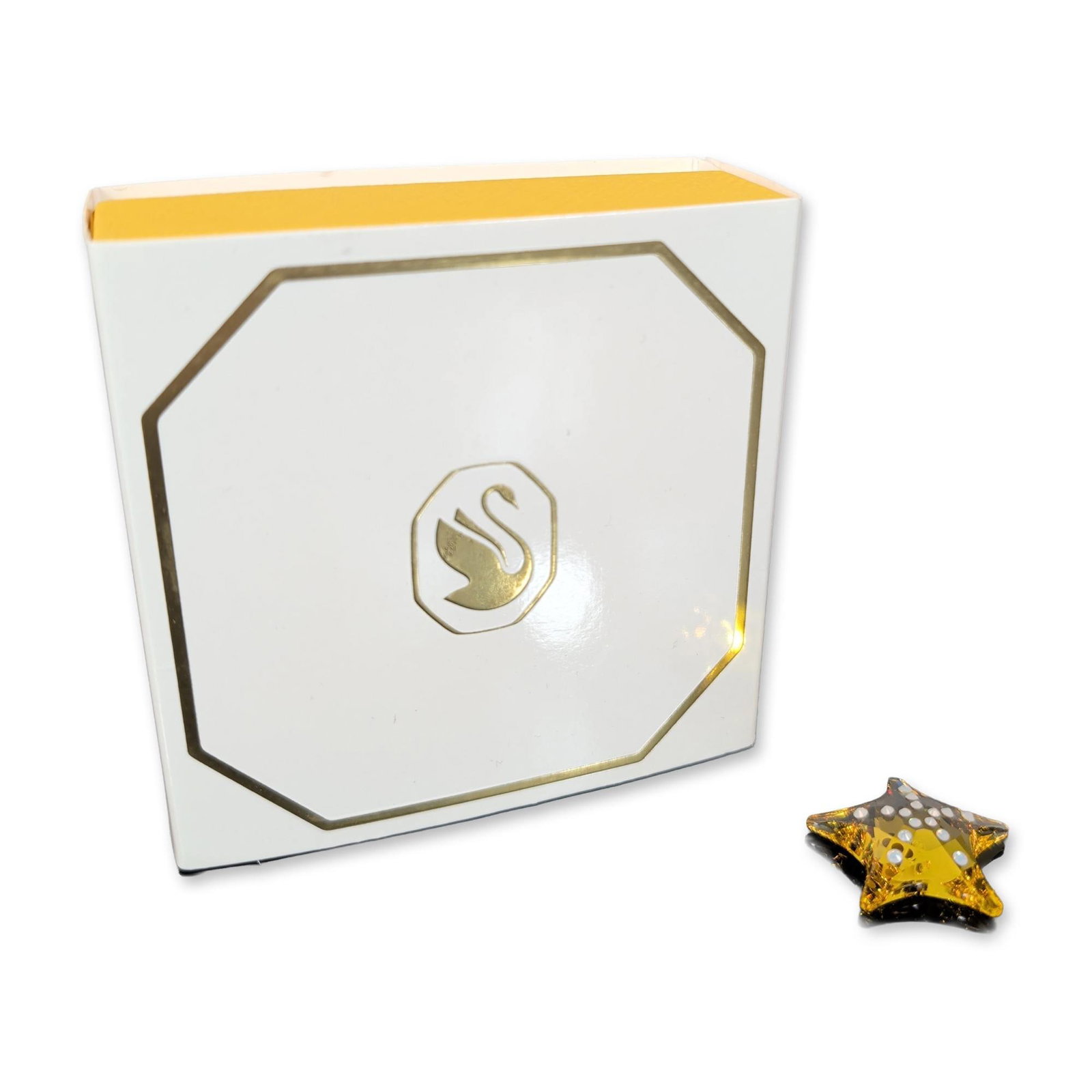 Swarovski Crystal SCS Membership Amber Starfish: Swarovski five-pointed star crafted from faceted amber crystal. The star is decorated with circular white accents and is secured to a black snap-clip mechanism. The crystal bears multiple etched styli