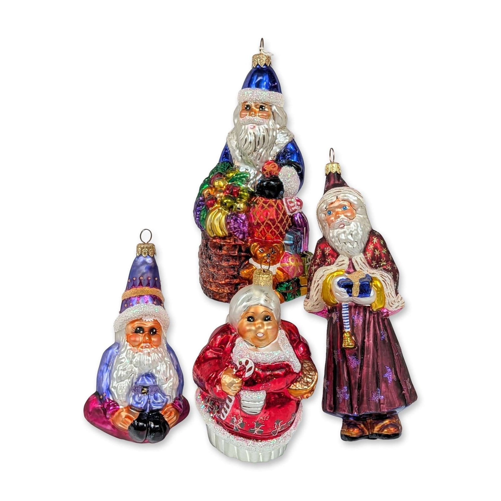 4pc Christopher Radko Collection of Glass Christmas Ornaments: The grouping includes a large Santa Delivers figure seated atop a basket of toys and fruit, a tall Santa in a maroon robe decorated with gold stars, a Mrs. Claus figure holding a tray of cookies and