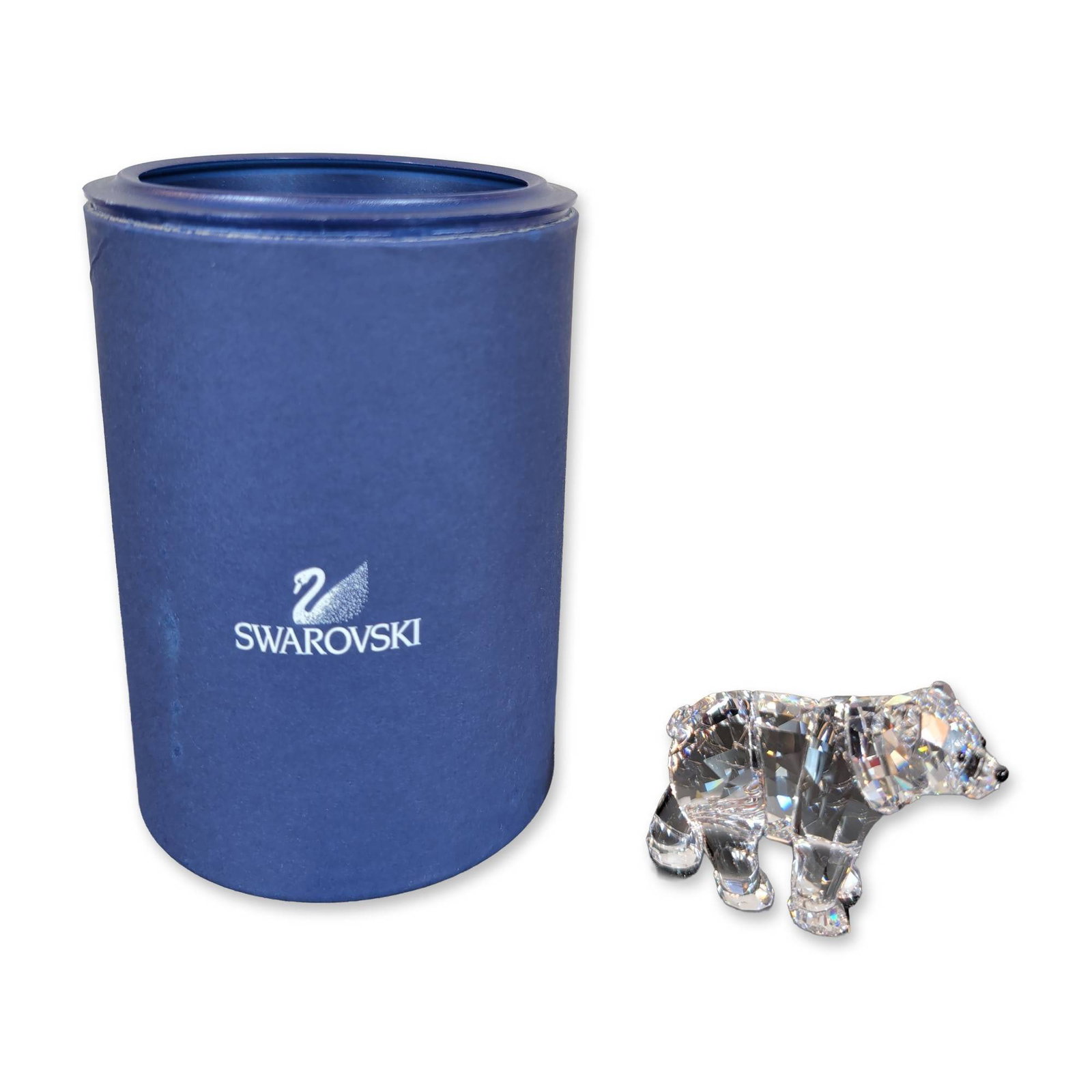 Swarovski Crystal Brother Bear Cub Figurine: Polar bear cub figurine in clear faceted lead crystal, with jet crystal eyes and nose. Etched swan logo present on the base. Accompanied by original dark blue cylindrical presentation box with